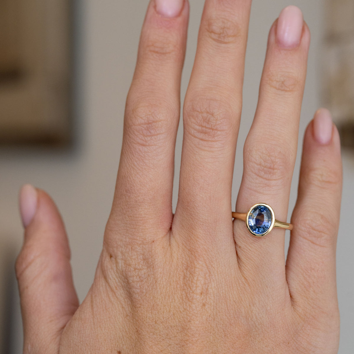 Blue sapphire solitaire engagement ring worn on the hand, showing the elegant proportions of its minimal antique-inspired design.