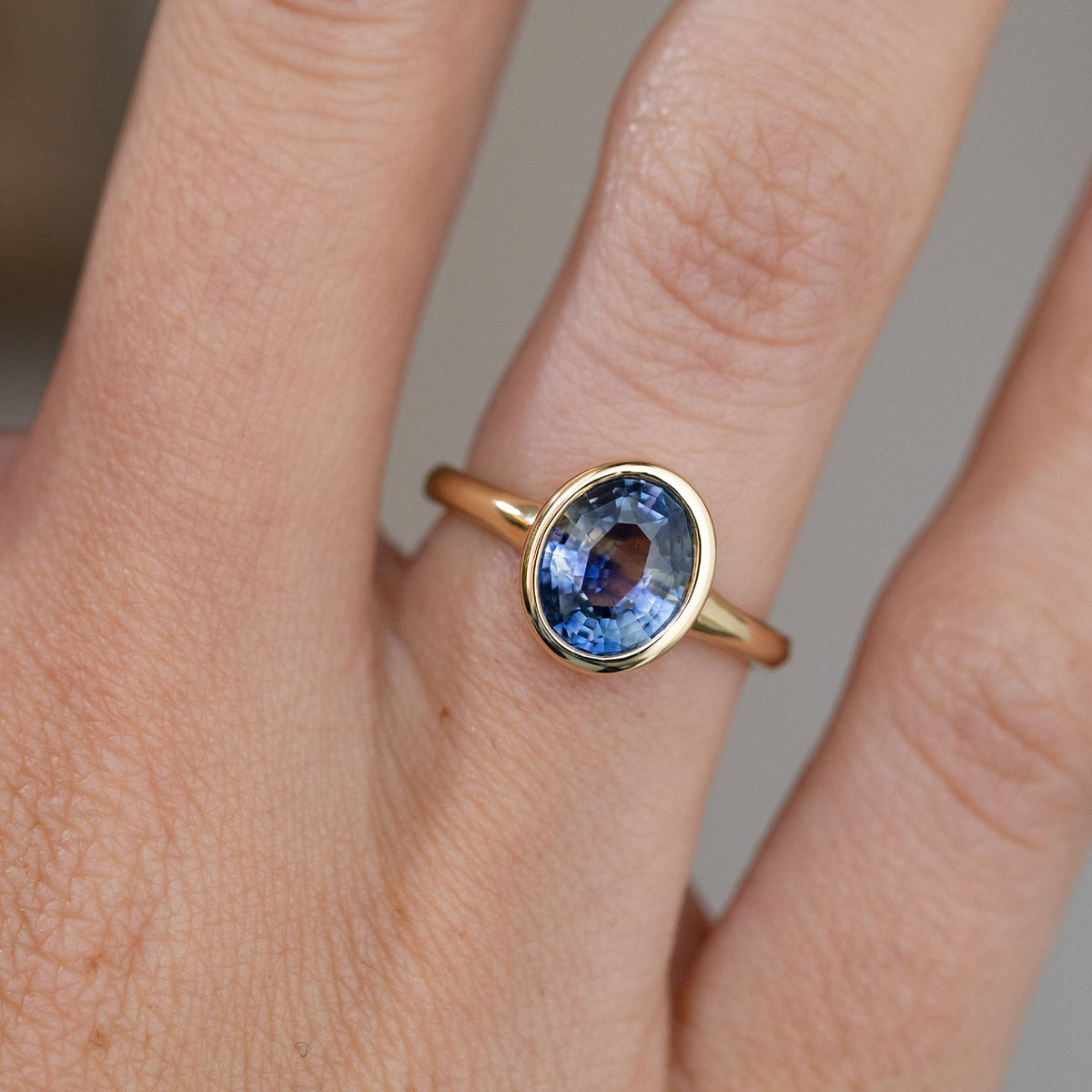 Detailed hand shot of the antique-inspired solitaire, capturing the sapphire’s natural colour variation and sleek gold surround.