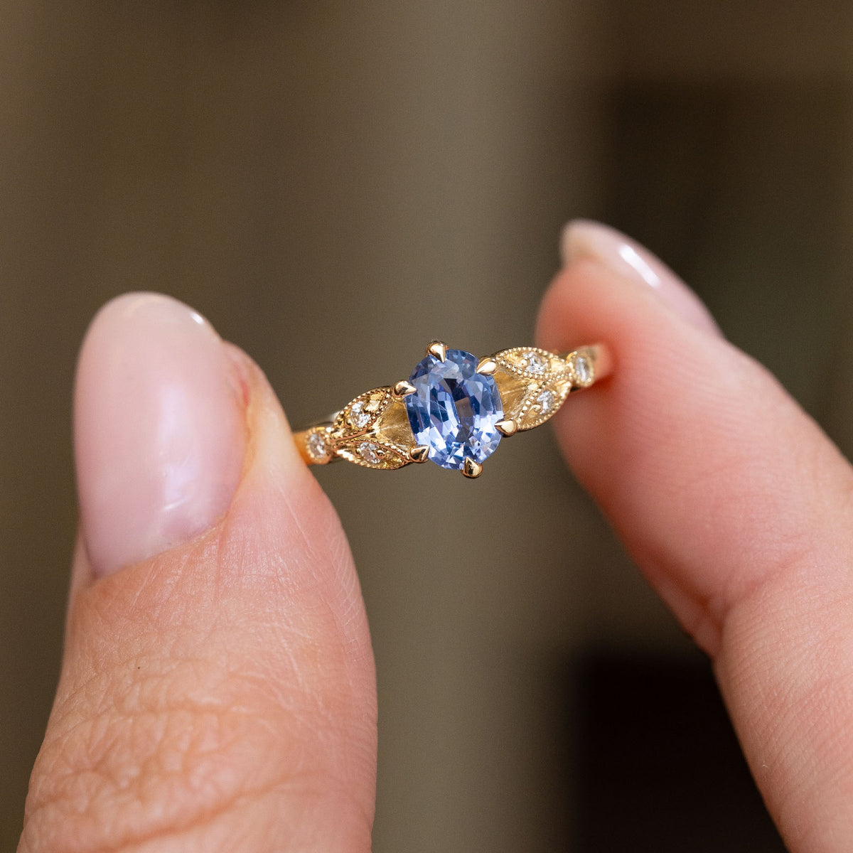 Handheld portrait of the oval-cut sapphire framed by sculpted leaf motifs and small sparkling diamonds.