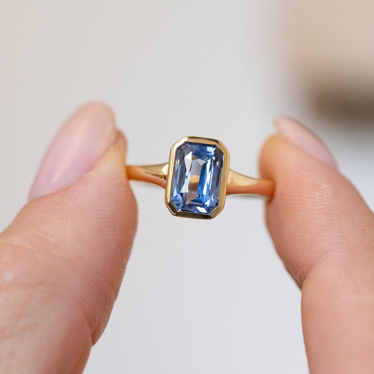 Handheld close-up of the rectangular sky-blue sapphire framed by a sleek polished gold surround.