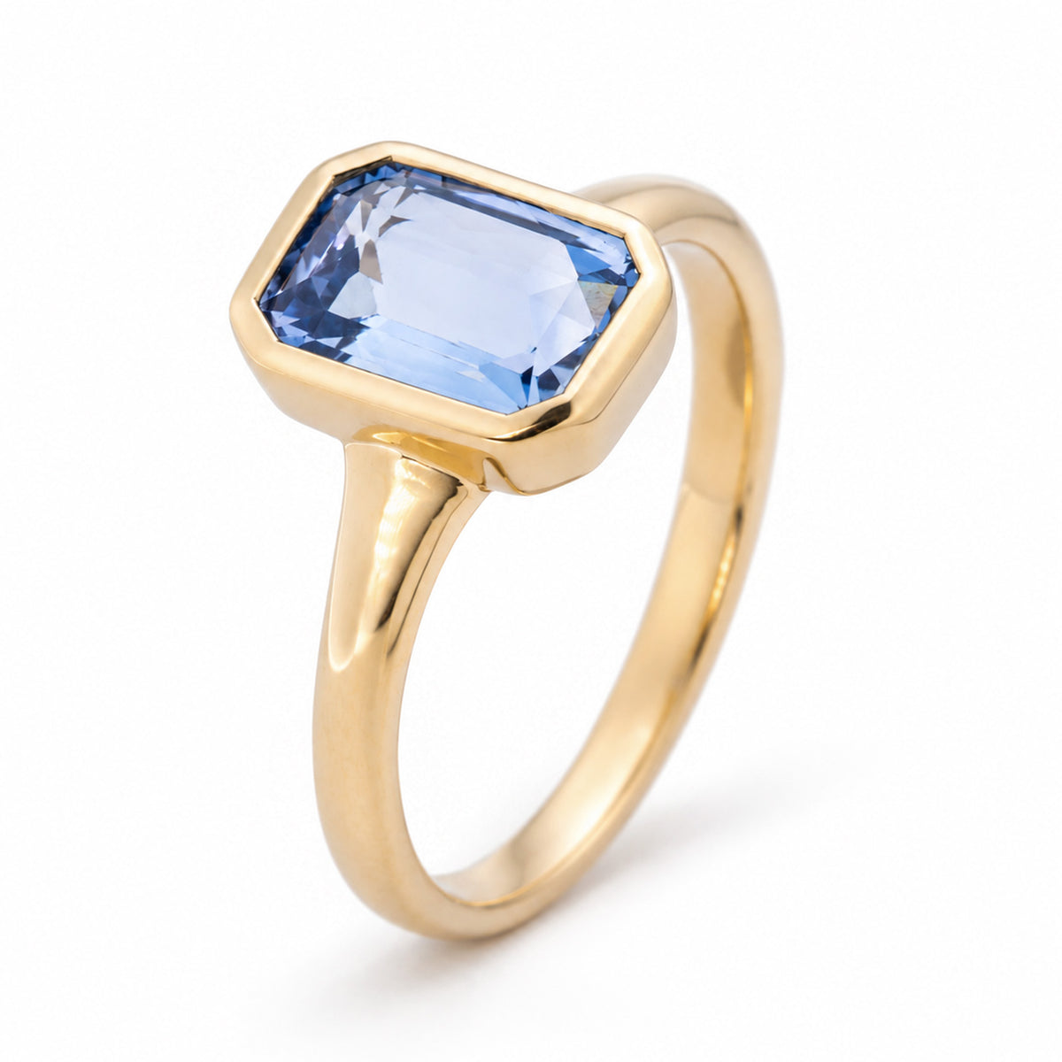 Raised studio portrait of the sky-blue sapphire ring, revealing its geometric silhouette, tapered shoulders and polished gold band.