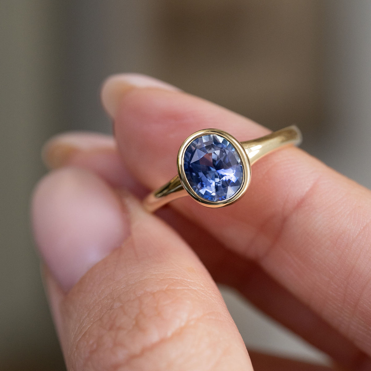 Handheld view of the oval blue sapphire in its minimal antique-inspired yellow gold setting.
