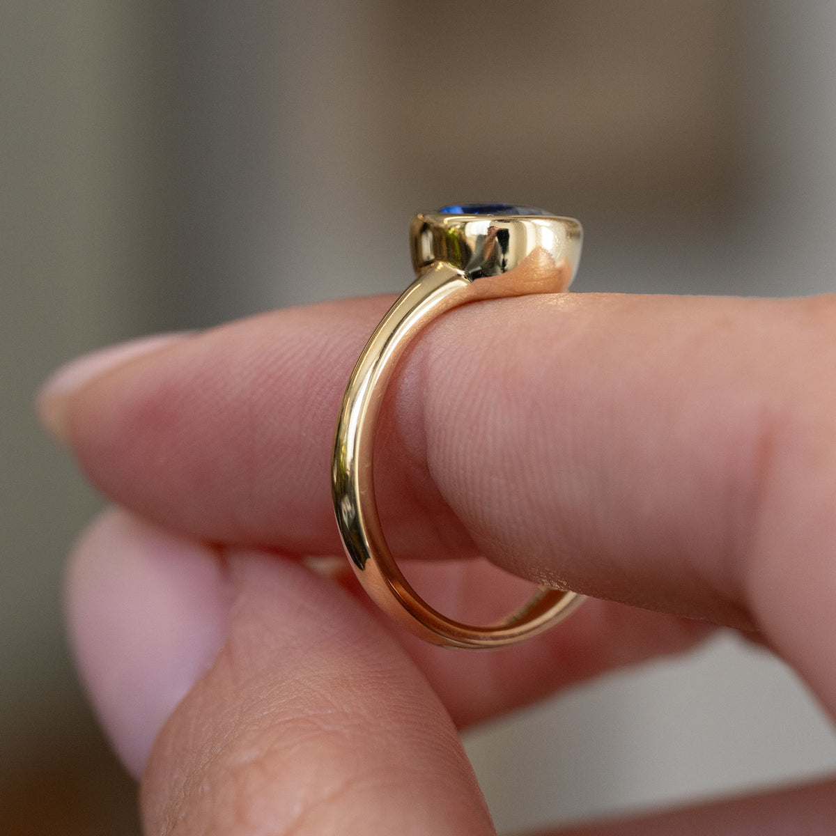 Side profile of the sapphire engagement ring, displaying its raised rub-over mount and slender polished shank.