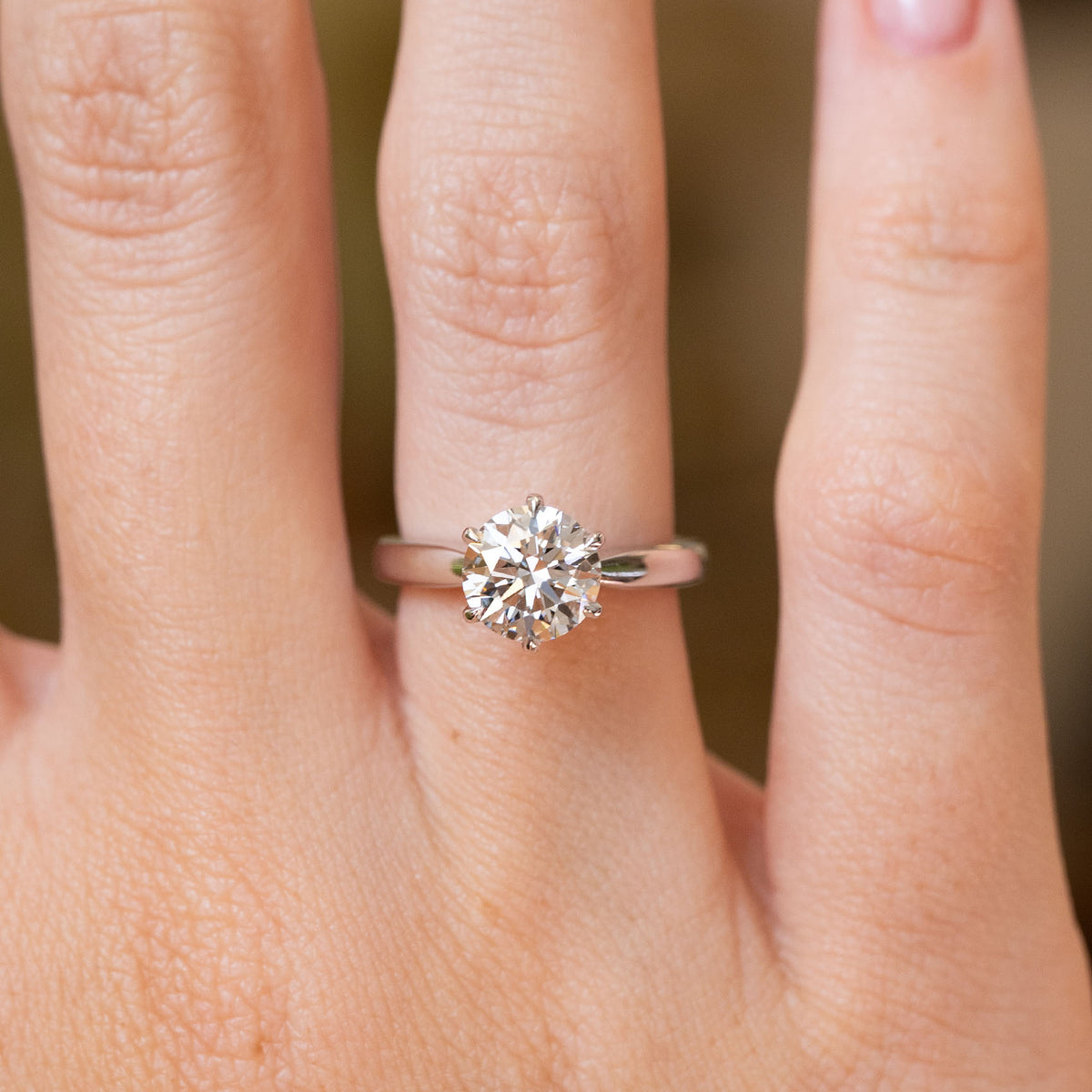 Close-up of a round brilliant-cut lab diamond engagement ring worn on the finger with a polished white gold band.
