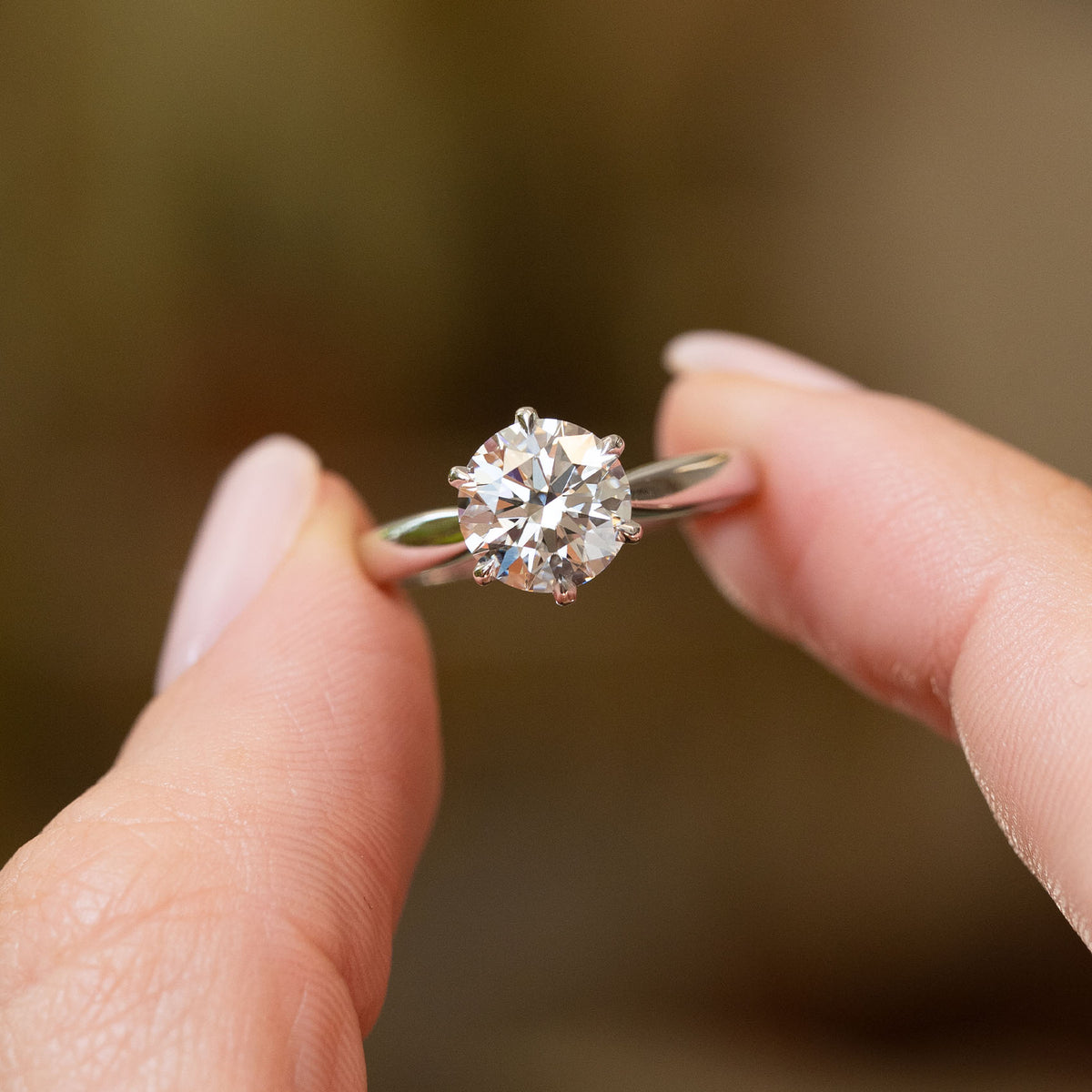 Vintage lab-grown diamond solitaire held between the fingers, showcasing its brilliant round cut and elegant white gold band.