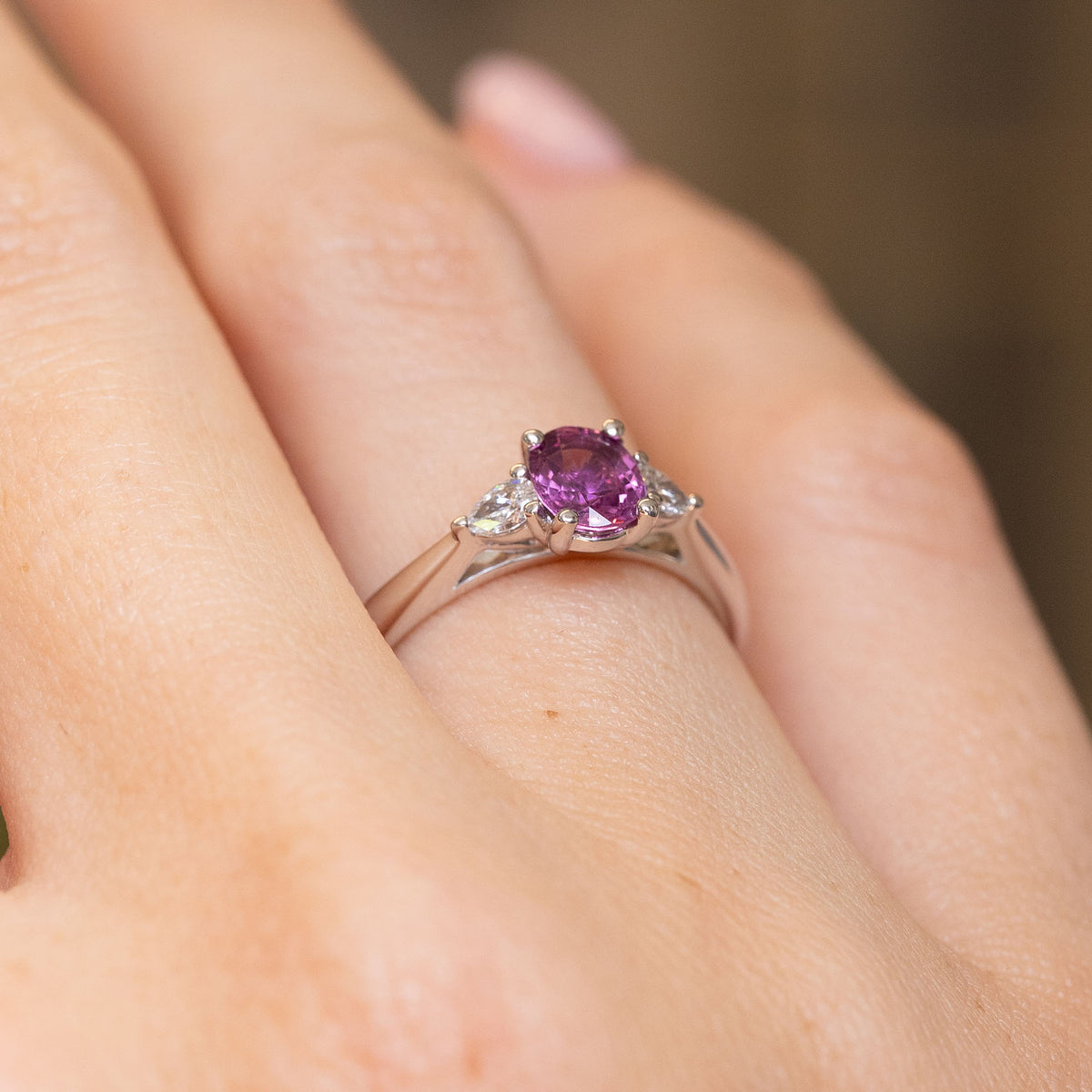 Side view of a purple-pink sapphire and diamond engagement ring worn on the hand, revealing the raised platinum claw setting.