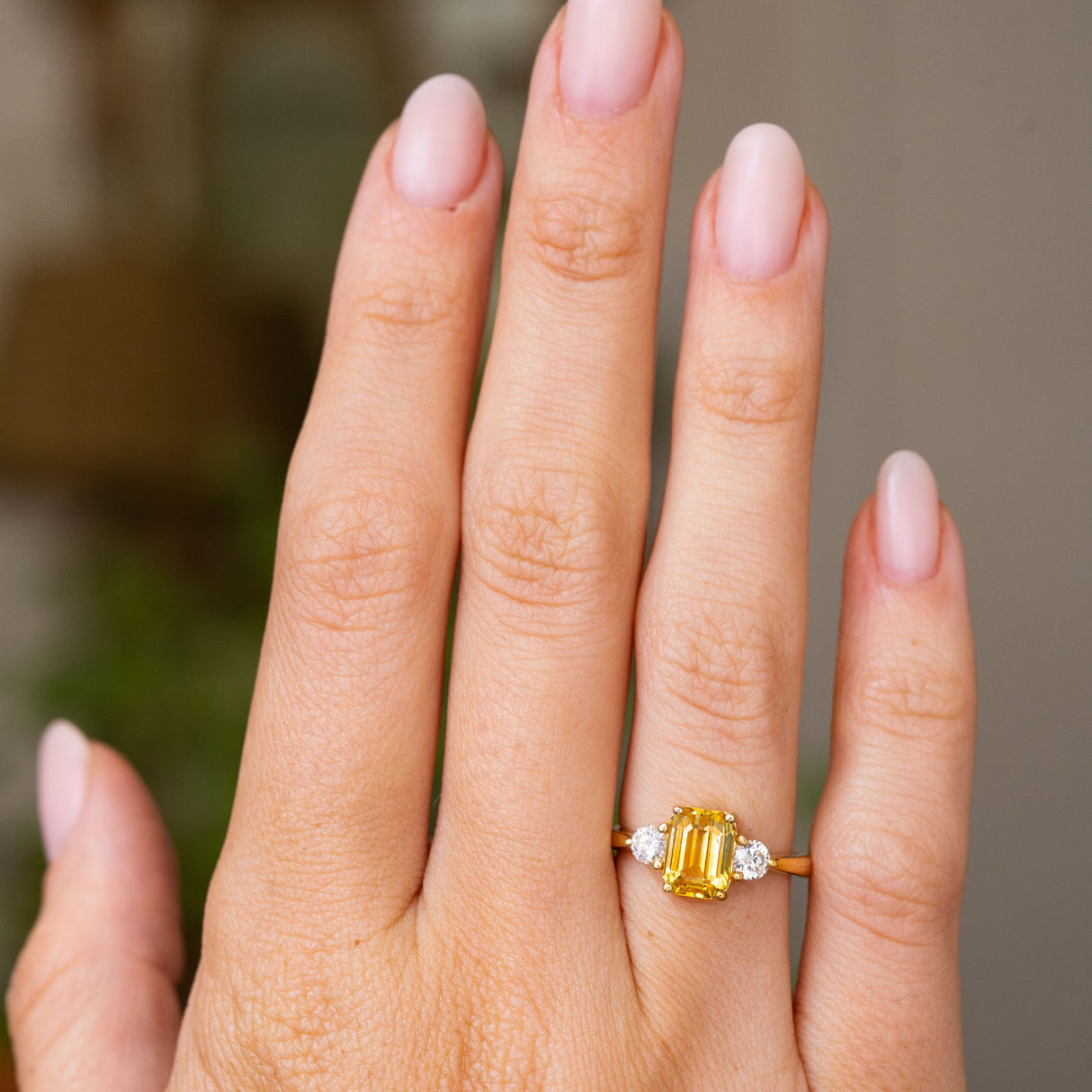 A hand wearing an antique-inspired, Yellow sapphire and diamond three-stone engagement ring in yellow gold shown at a distance