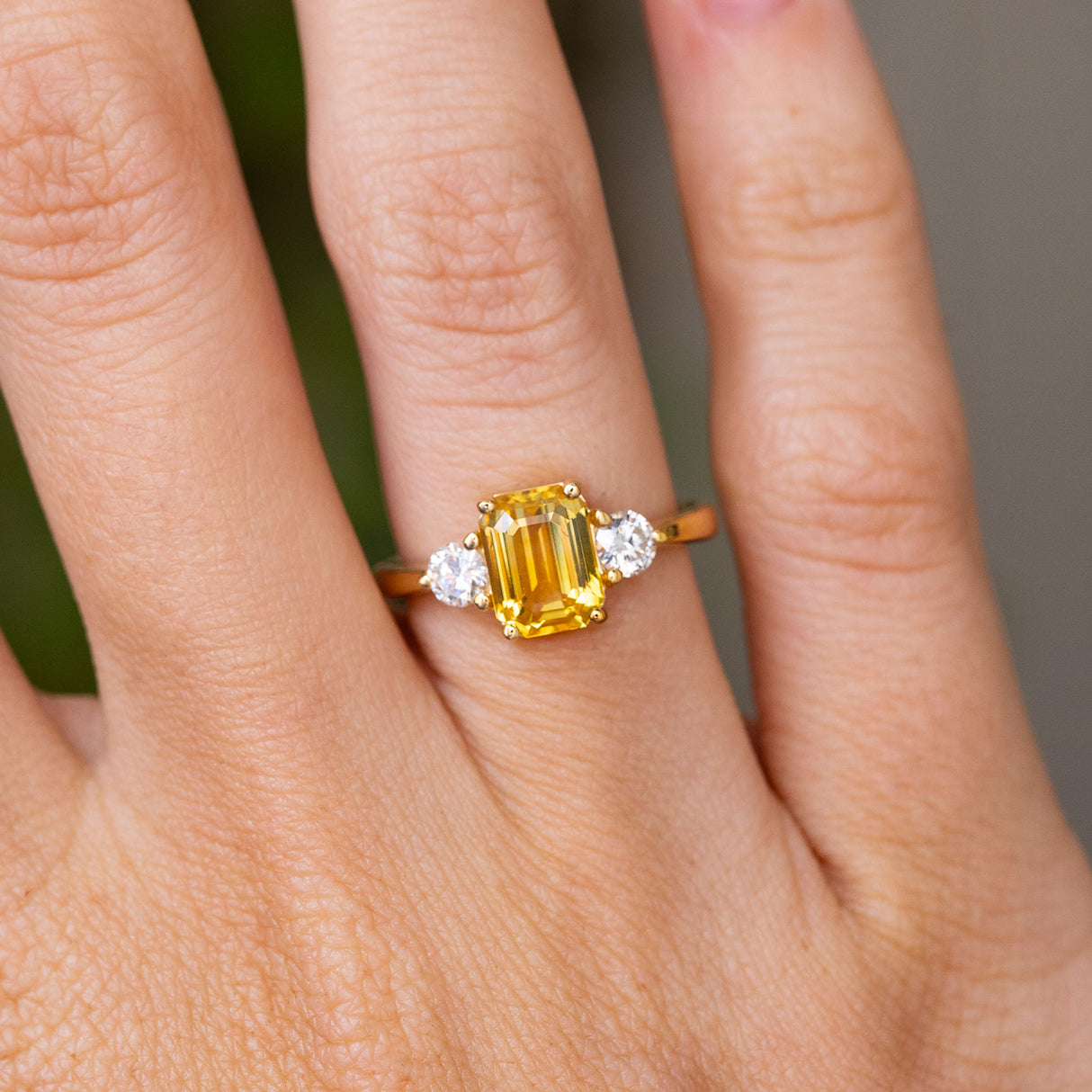 A close up image of a hand wearing an Antique-inspired, Yellow sapphire and diamond trilogy yellow gold engagement ring
