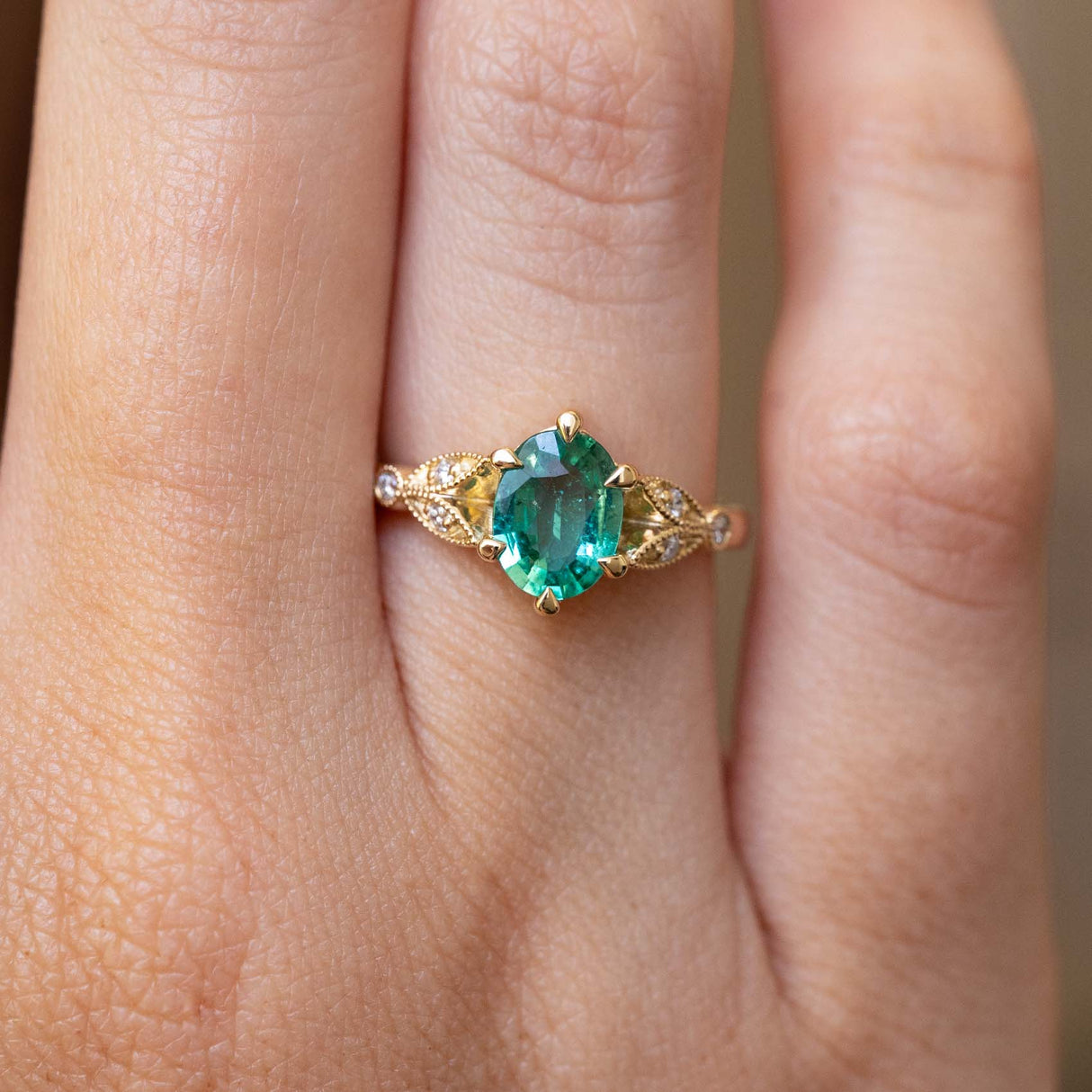 A close-up of a Vintage-inspired, Emerald and diamond engagement ring in yellow gold worn on a finger.