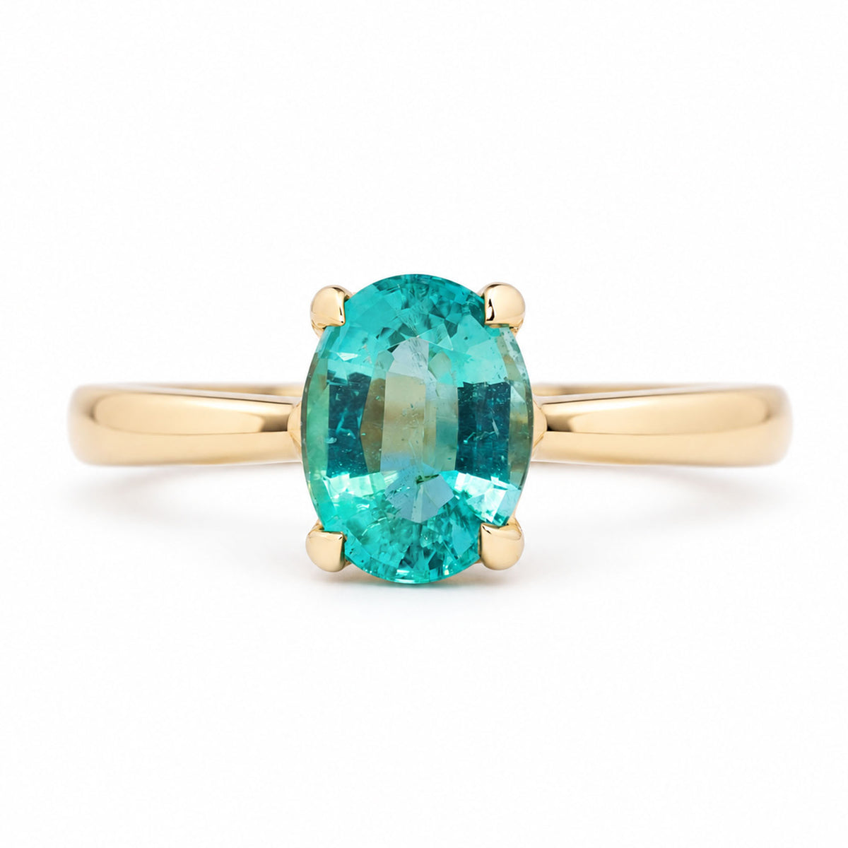 A close up of an Antique-inspired, solitaire engagement ring, featuring an oval-cut emerald claw set in a yellow gold band, photographed against a seamless white background.