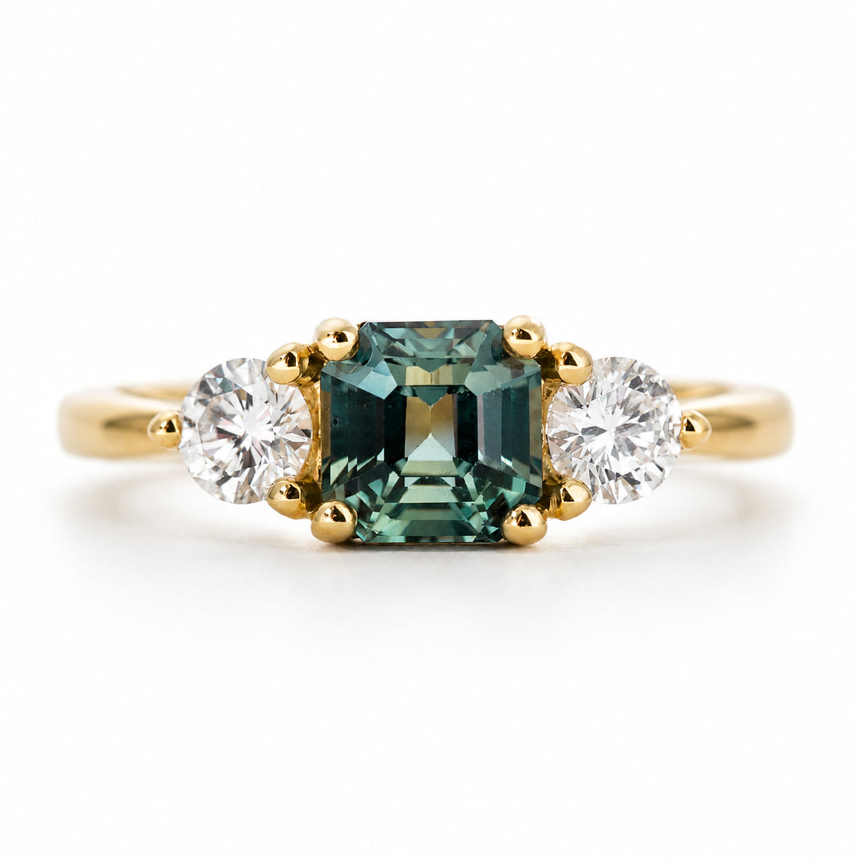 An antique-inspired yellow gold engagement ring set with a green sapphire at the centre, flanked by a diamond on each side.