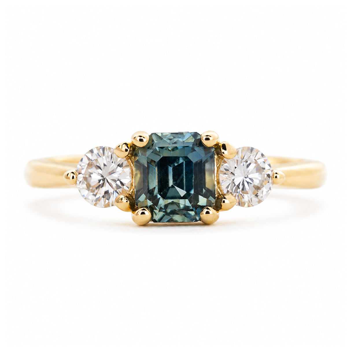 An antique-inspired engagement ring with a teal sapphire at the centre with a round brilliant-cut diamond on each side.