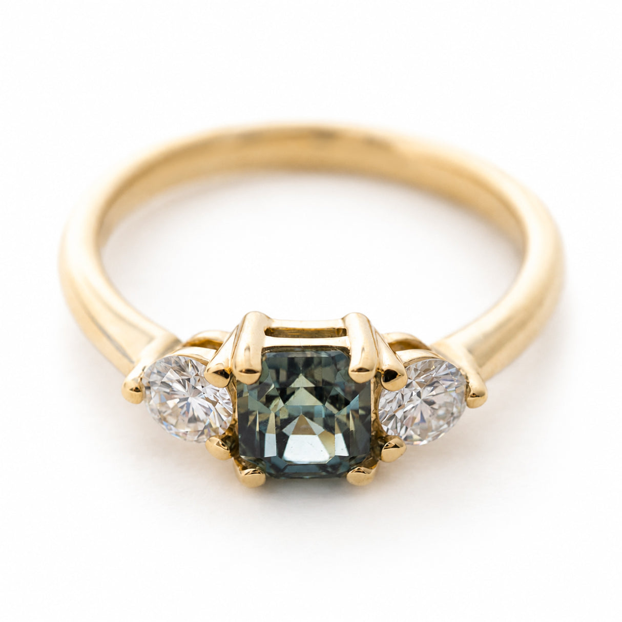 A vintage-inspired yellow gold engagement ring with a teal-green sapphire and diamond three-stone.