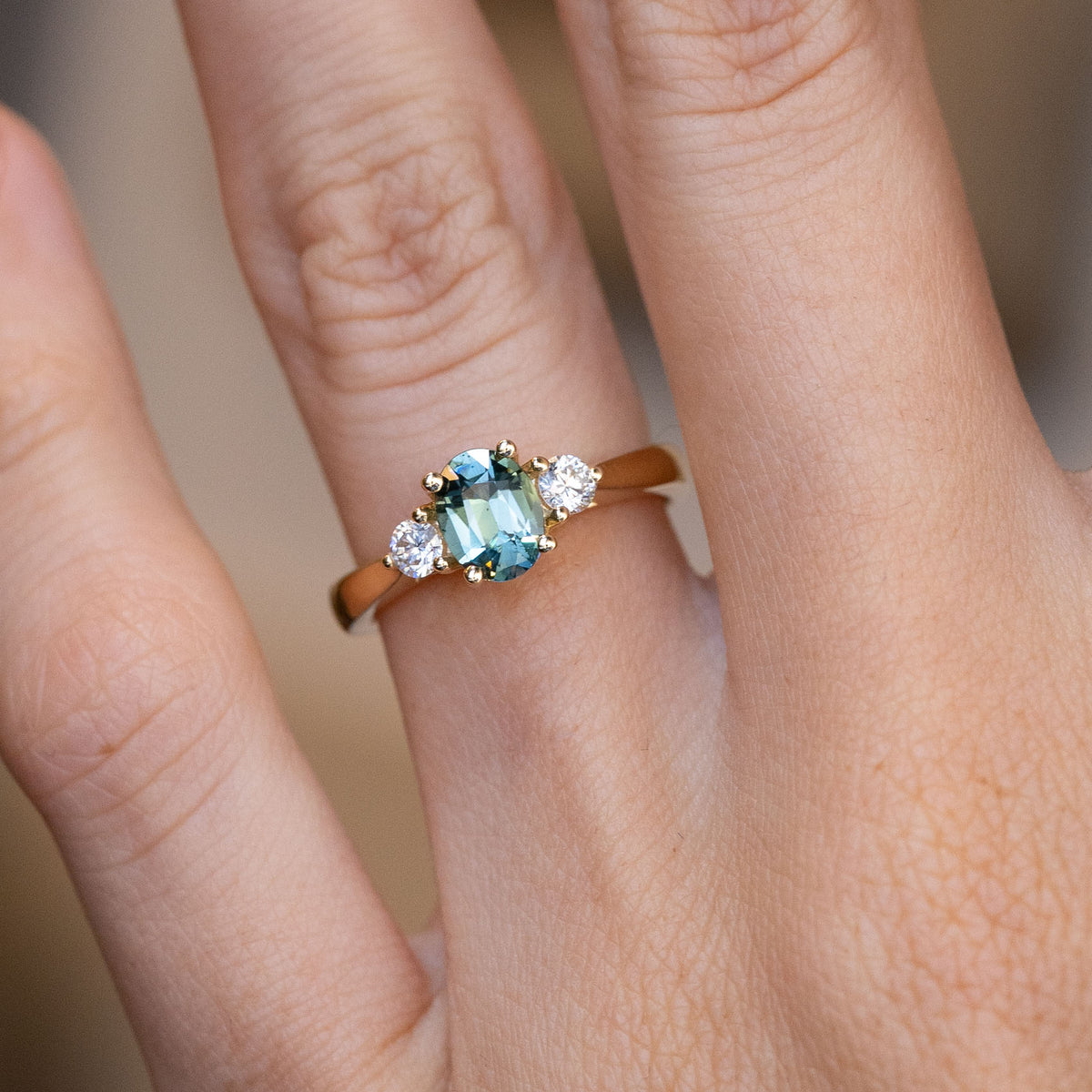 Close-up of the oval teal sapphire flanked by two sparkling white diamonds, worn on a finger.