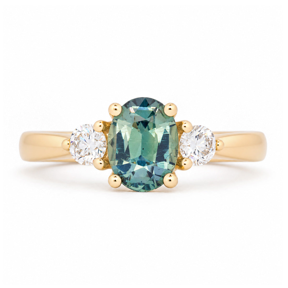 Antique-inspired teal oval sapphire and diamond three-stone engagement ring in yellow gold, featuring two round brilliant-cut diamond shoulders.