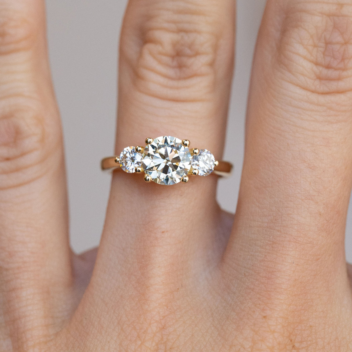 Close-up of the three-stone diamond ring on a finger, featuring a pale yellow centre diamond and white diamond shoulders.