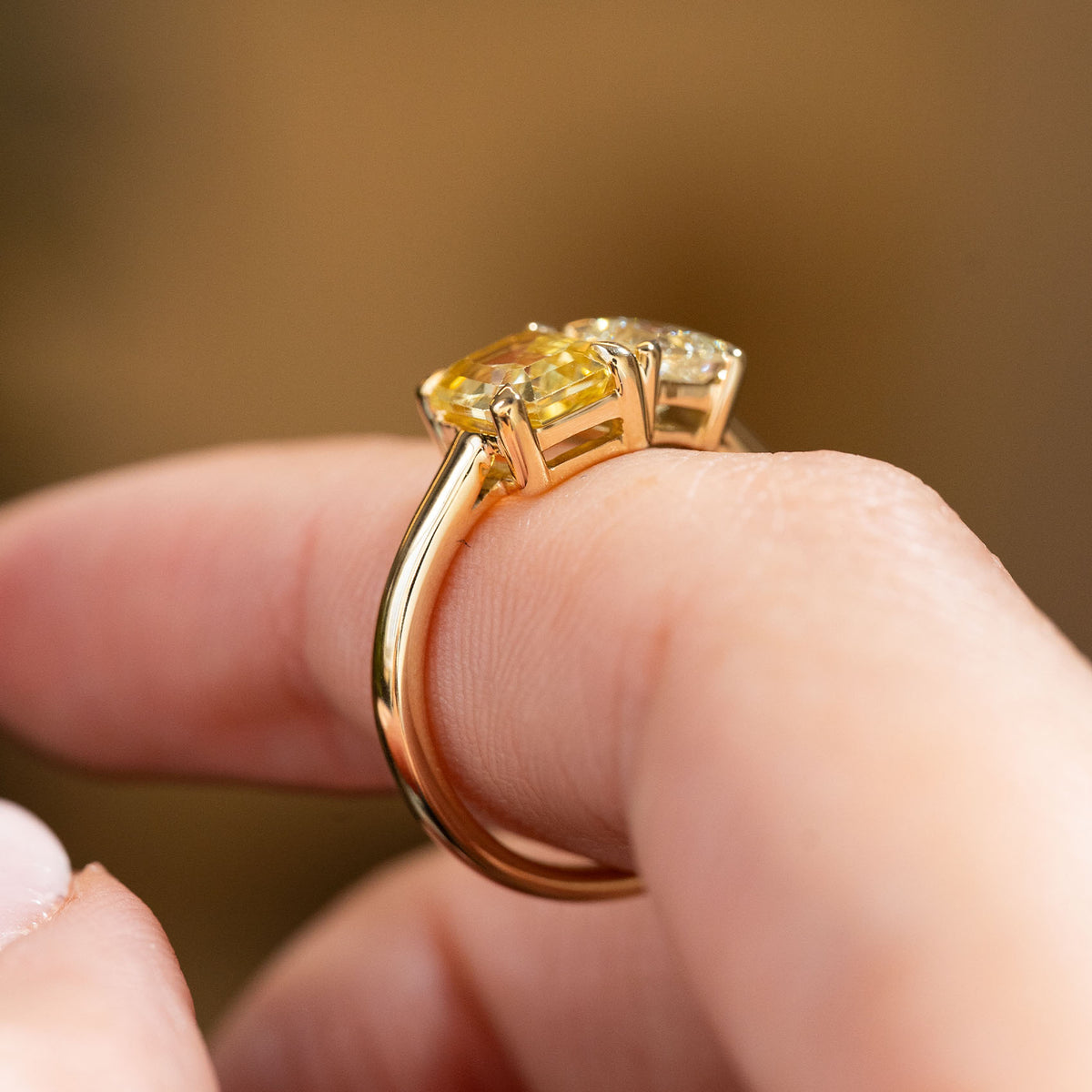 A close-up of an Antique-inspired, Diamond and yellow sapphire Toi et Moi engagement ring in yellow gold worn on a finger and shown from the side to display the profile and shank
