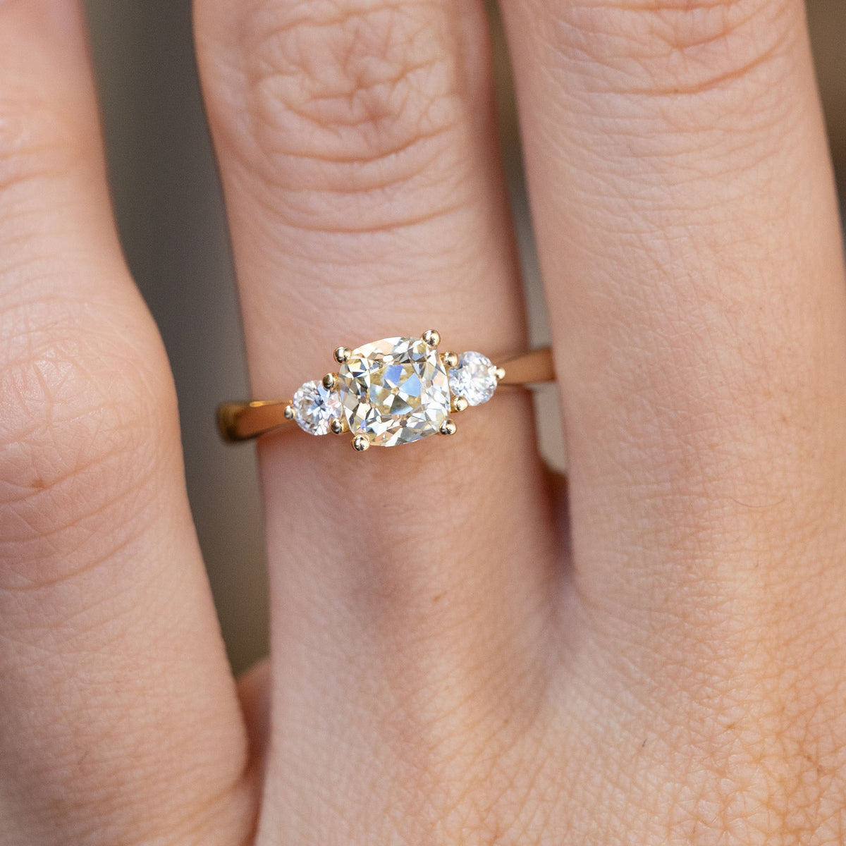 Close-up of the cushion-cut centre diamond flanked by two round brilliant-cut diamonds, worn on a finger.