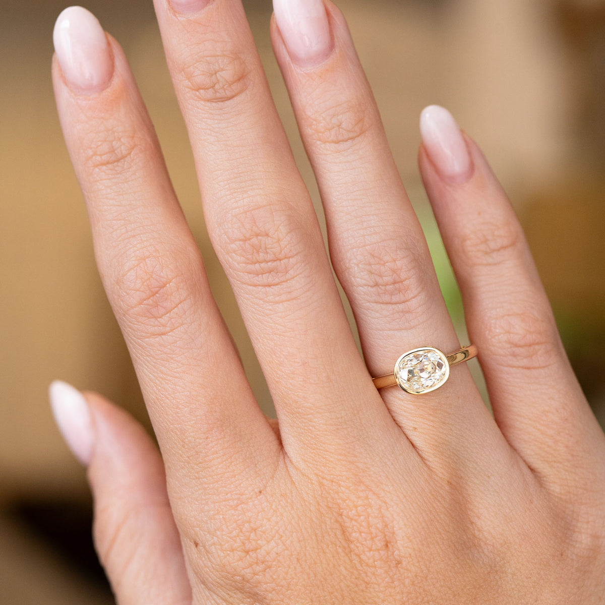 Antique-inspired diamond solitaire engagement ring worn on the hand, showcasing its elongated cushion old-mine cut and slim gold band.