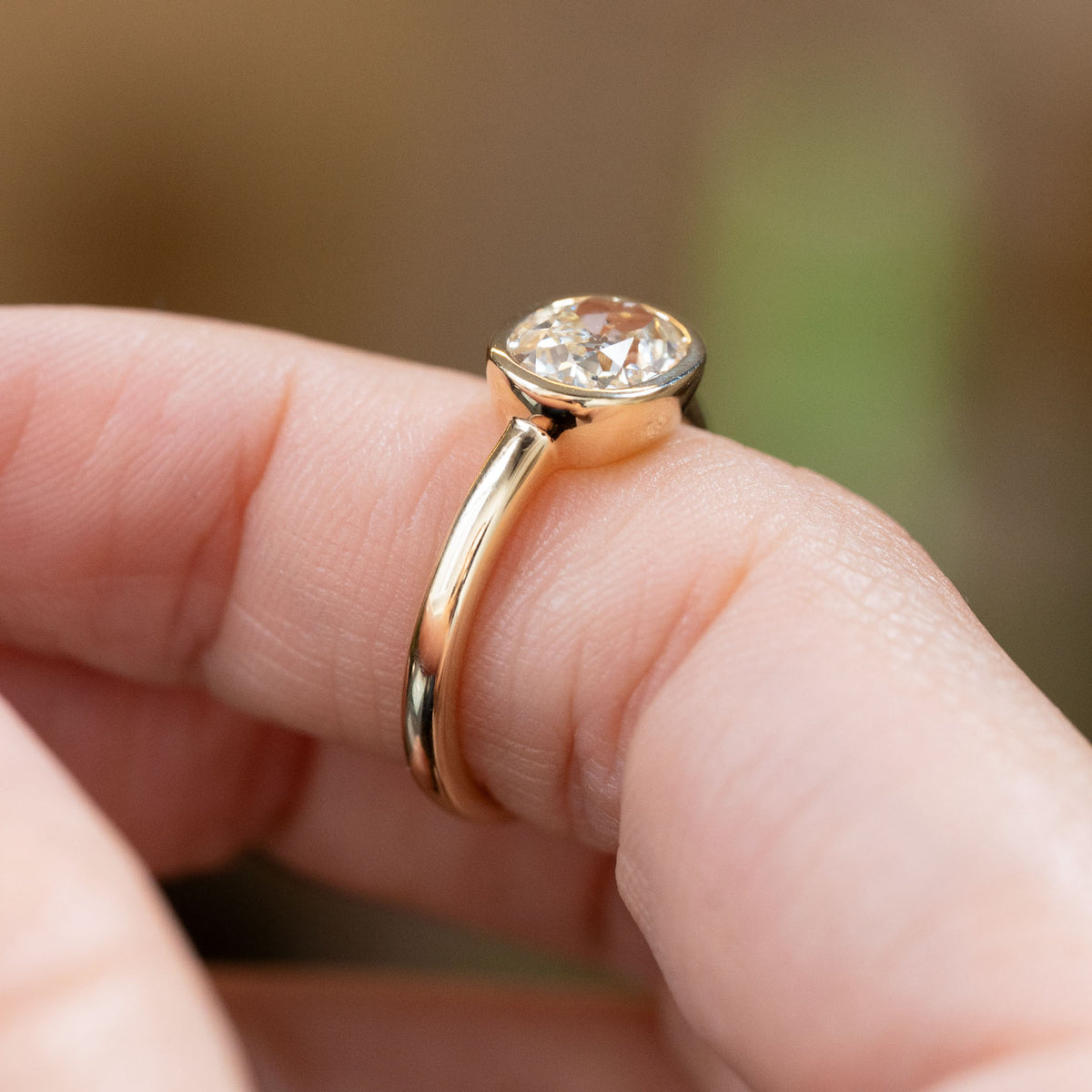 Profile view of an antique-style old-mine cut diamond solitaire ring, highlighting the elevated rub-over setting and polished yellow gold band.