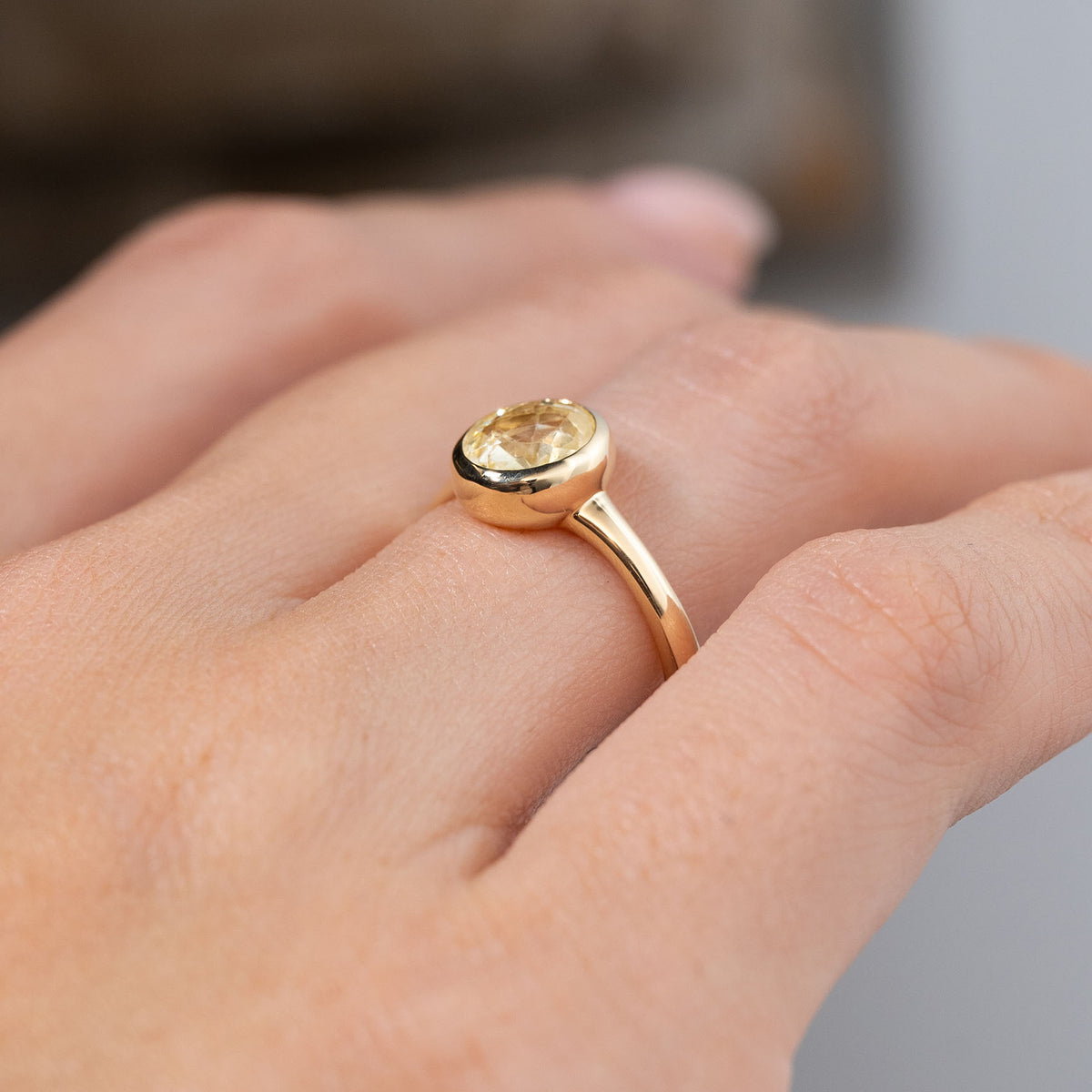 Angled side view of an antique-inspired pale yellow sapphire solitaire engagement ring worn on a hand, showing the raised oval bezel setting and gently curved yellow gold band.