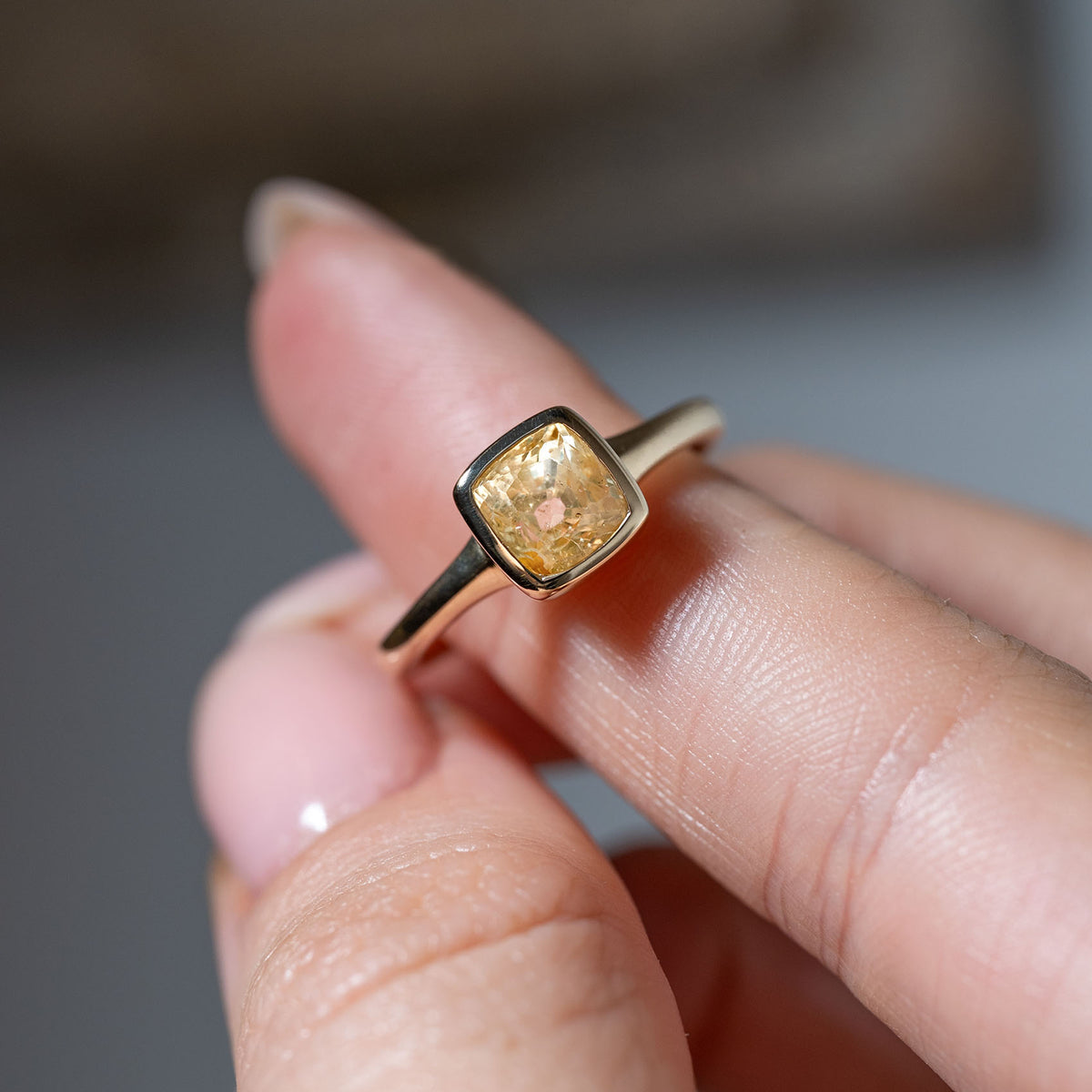 Detailed angled view of the cushion-cut yellow sapphire ring held between fingers, showcasing its warm colour and minimalist antique-inspired design.