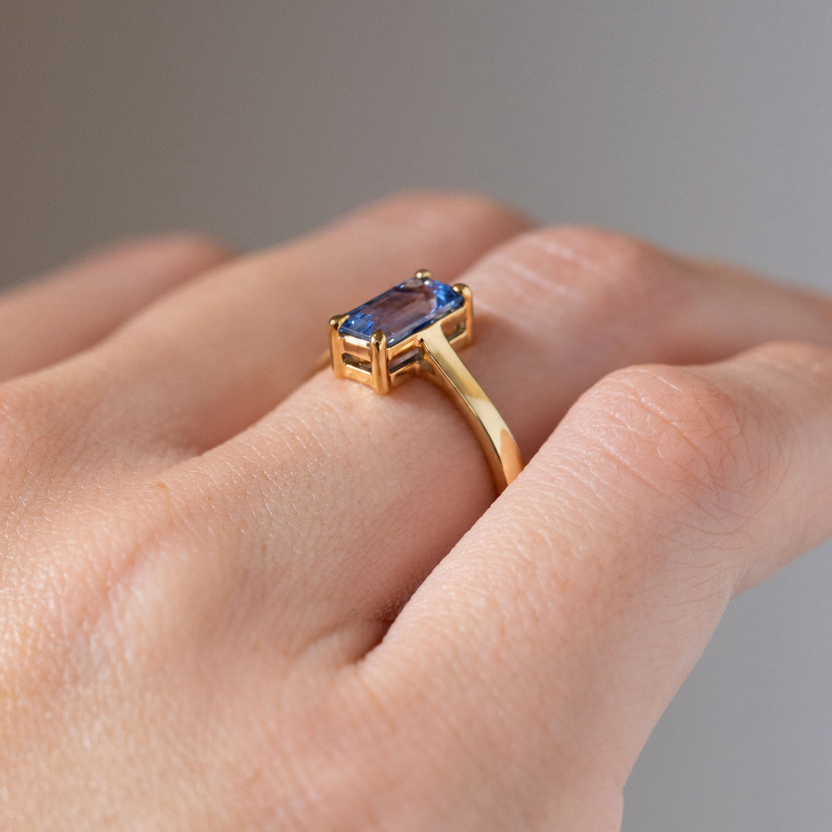 Side angle of the blue sapphire engagement ring worn on a finger, revealing its raised open gallery and slender yellow gold band.