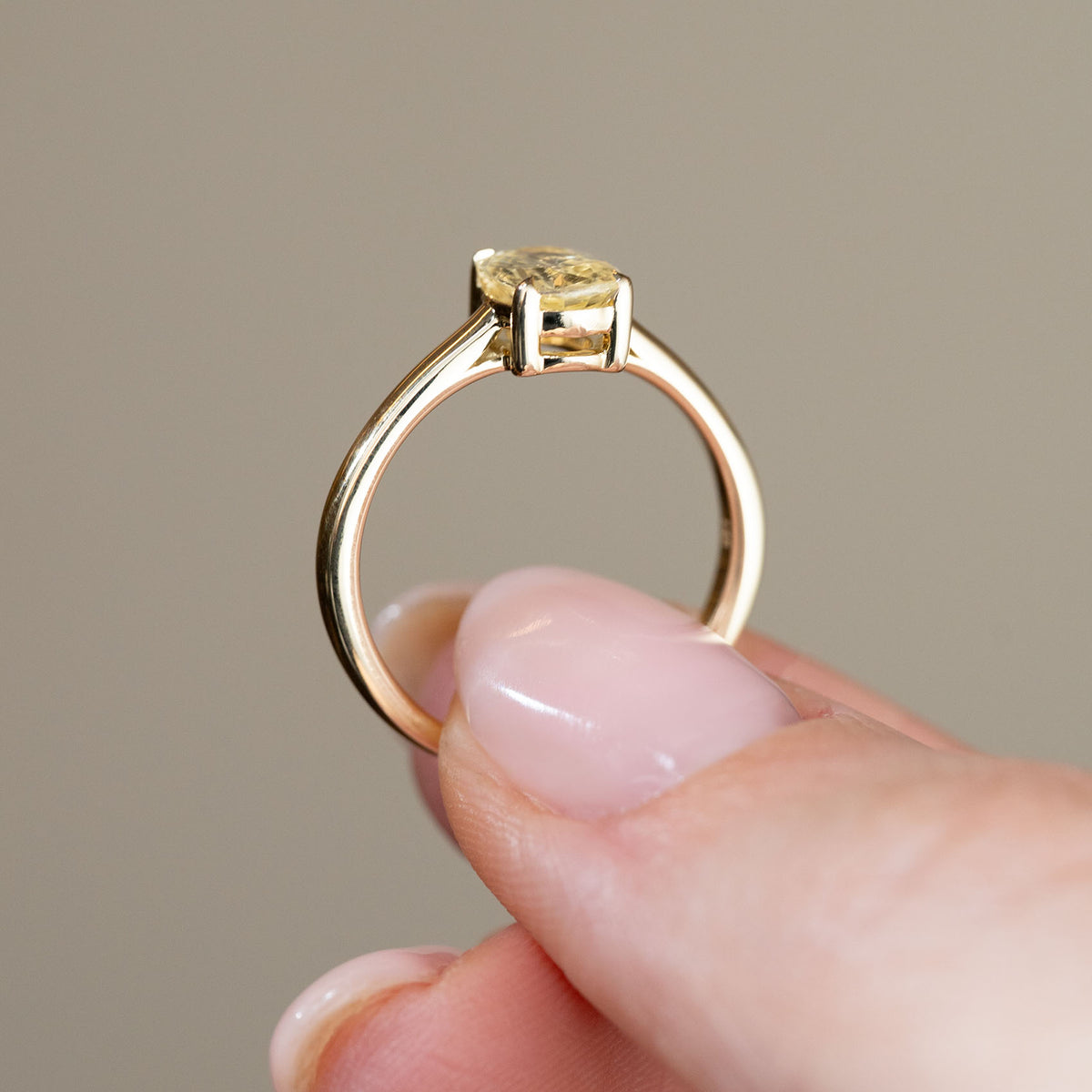 Rear profile of the antique-style solitaire ring held between fingers, showcasing the open gallery beneath the sapphire and slim yellow gold shank.