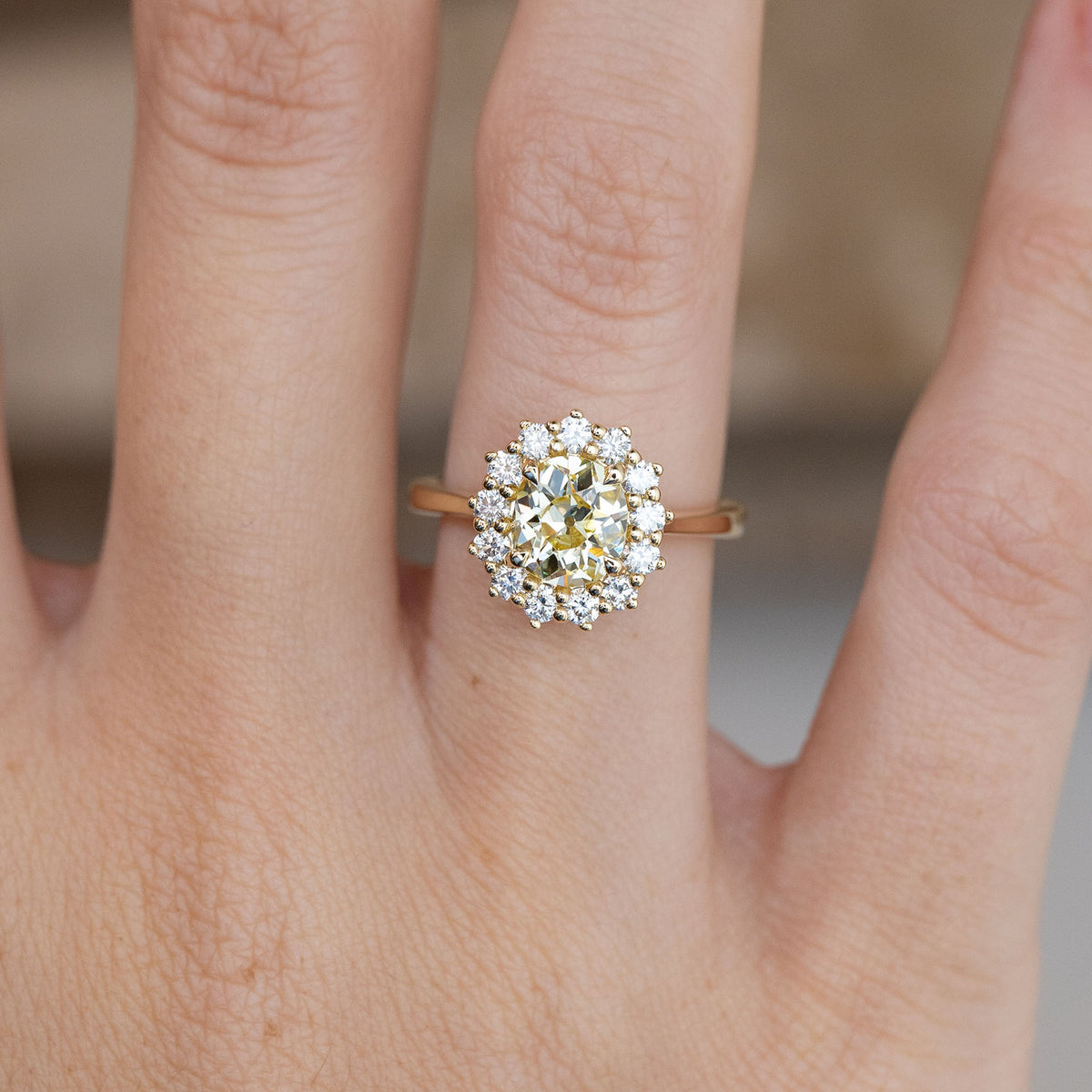 Close-up of the cushion old-mine cut yellow diamond surrounded by brilliant-cut white diamonds, worn on a finger.