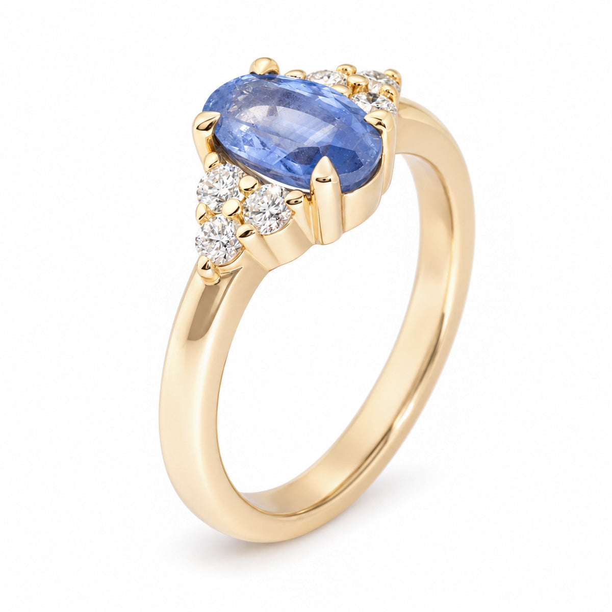 Angled studio photograph of a yellow gold engagement ring with an oval blue sapphire and delicate diamond trefoil detailing on either side.