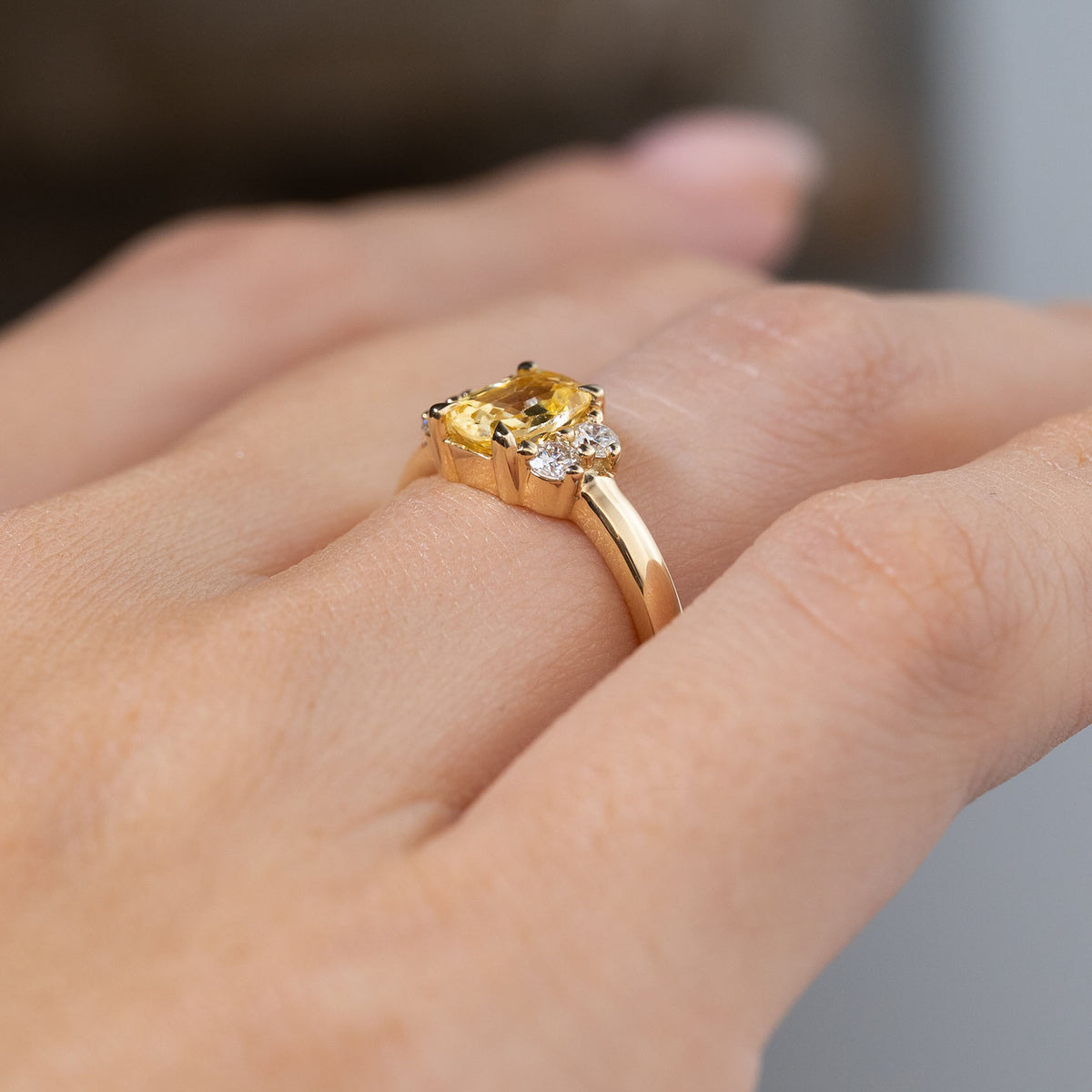 Angled side view of the yellow sapphire and diamond cluster engagement ring worn on a finger, revealing its raised claw setting, diamond accents and slender yellow gold band.
