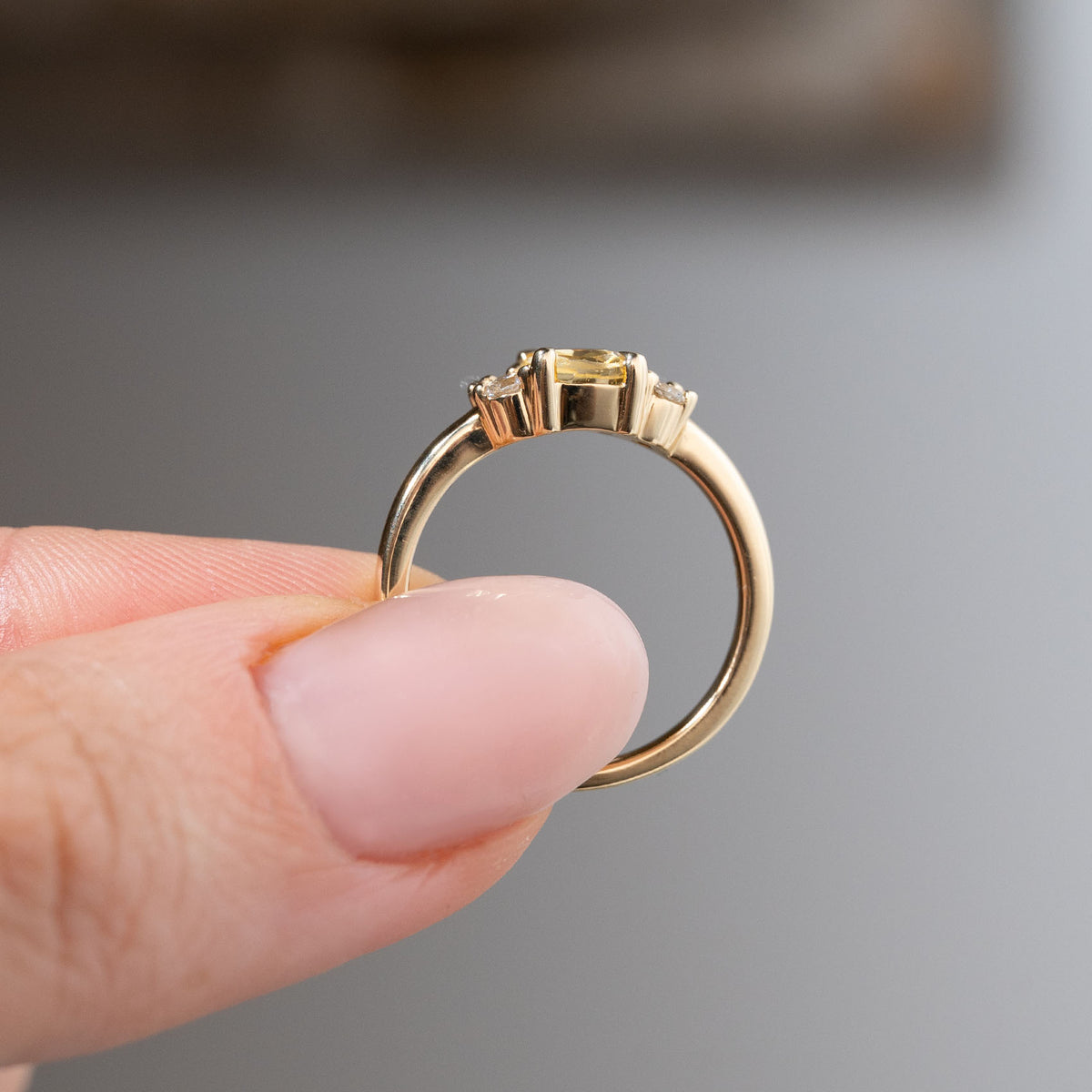 Side profile of the yellow sapphire and diamond cluster engagement ring held between fingers, showcasing its elevated gemstone setting, open gallery and polished yellow gold band.