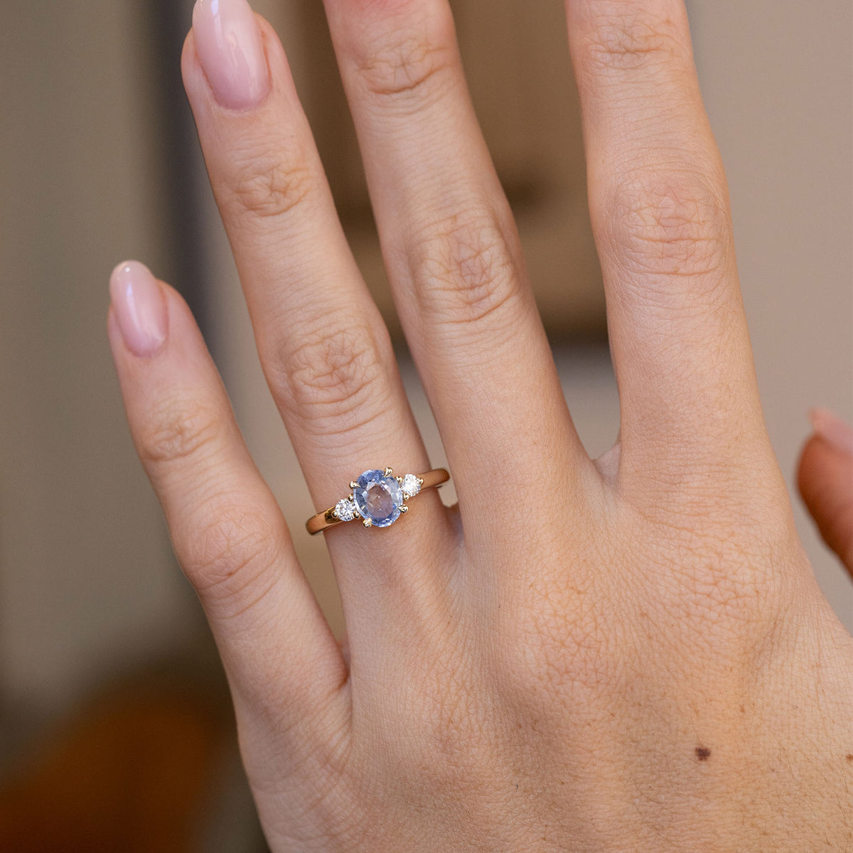 Blue sapphire three-stone engagement ring worn on a hand, showcasing its delicate proportions and classic design.