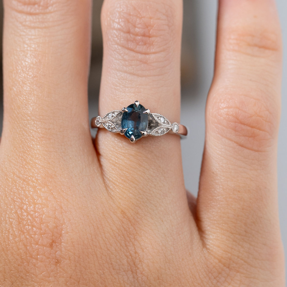 Close-up of the ring worn on a finger, showcasing the oval-cut sapphire, polished platinum claws and sparkling diamonds within the trefoil design.