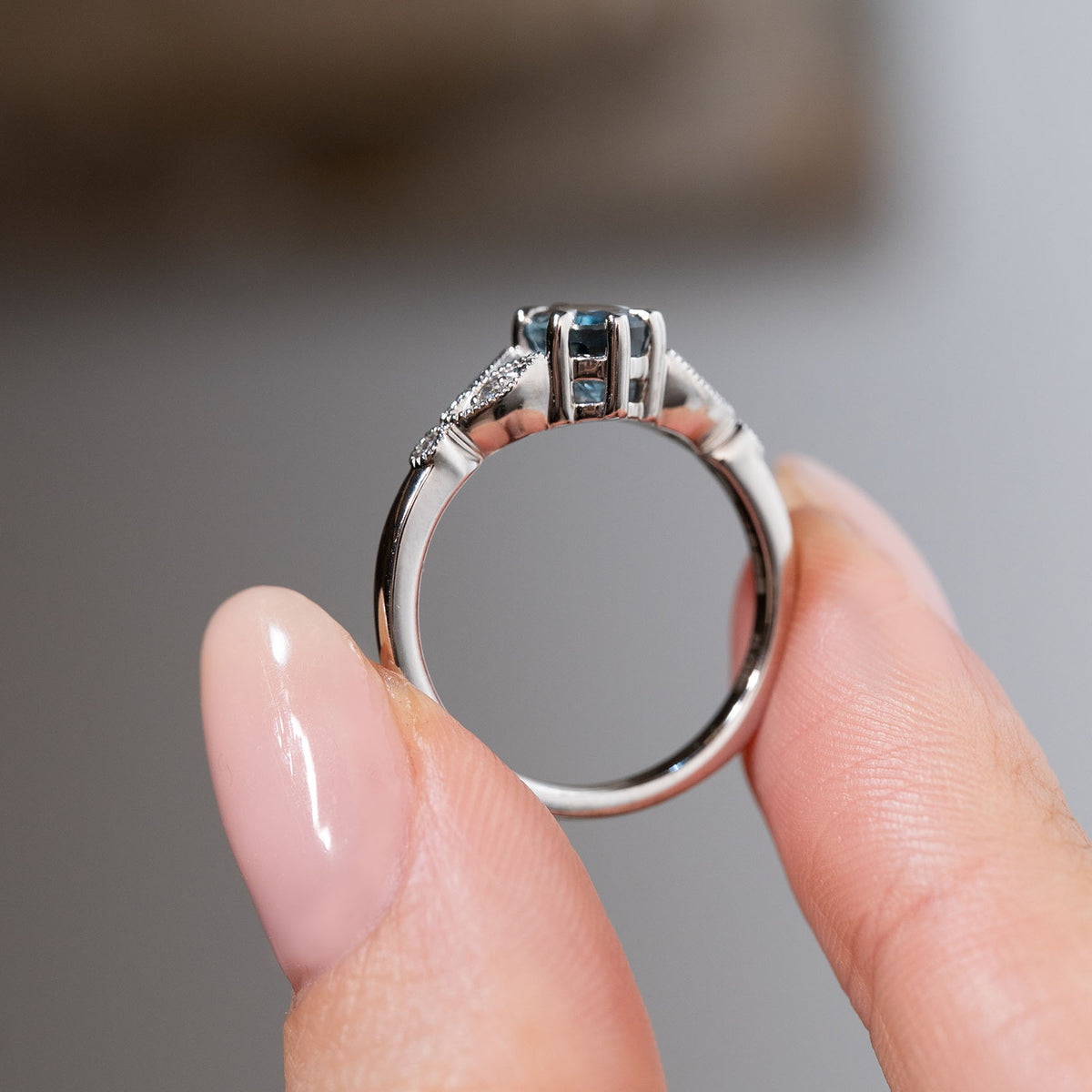 Side profile of the sapphire engagement ring held between fingers, showcasing the elevated claw setting, open gallery and polished platinum band.