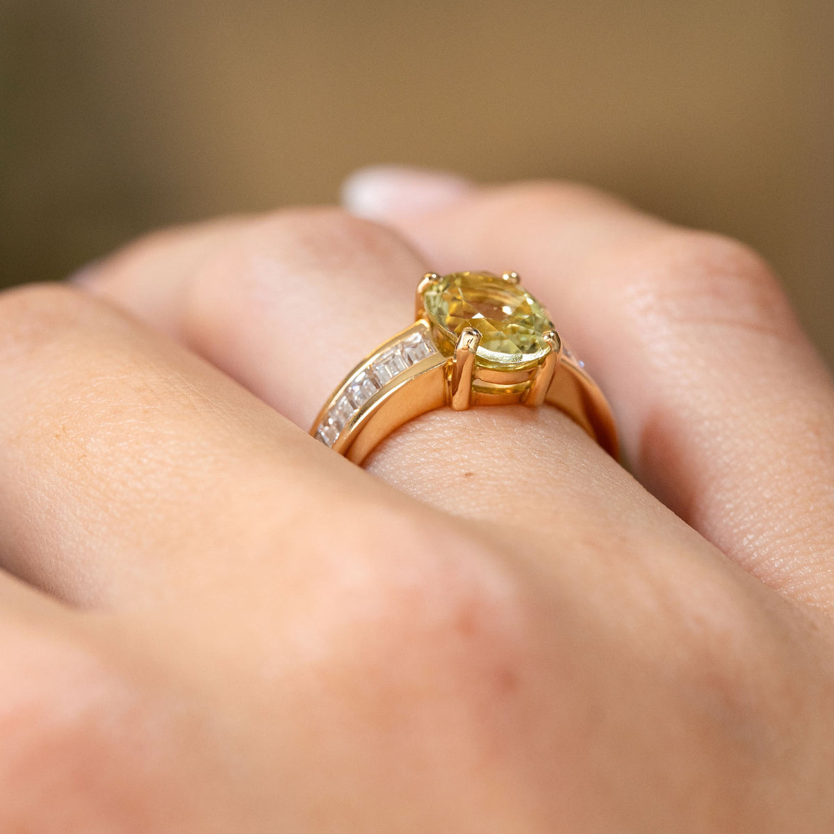 Side view of a vintage green beryl engagement ring worn on the hand, revealing the raised claw setting and diamond-set gold shoulders.