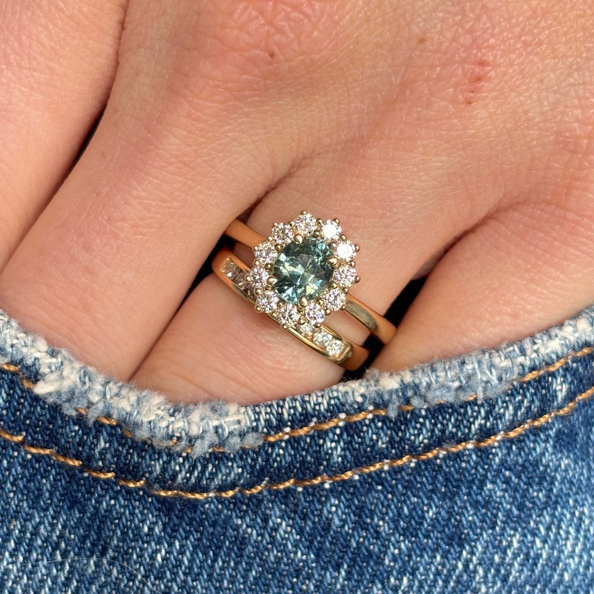 Green sapphire and diamond cluster engagement ring worn with wedding band to show scale.