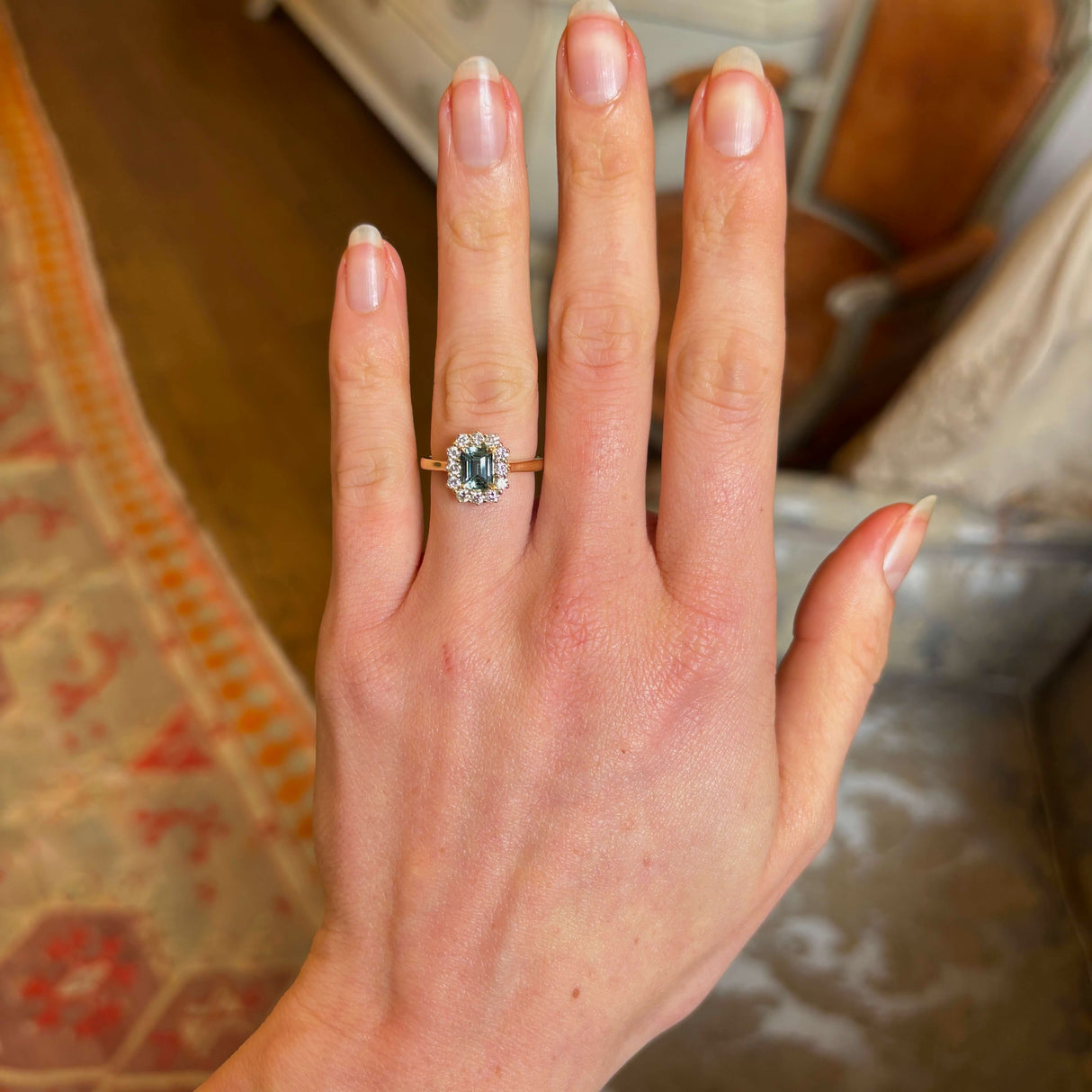 A yellow gold green sapphire and diamond cluster engagement ring worn on hand to show size and scale.