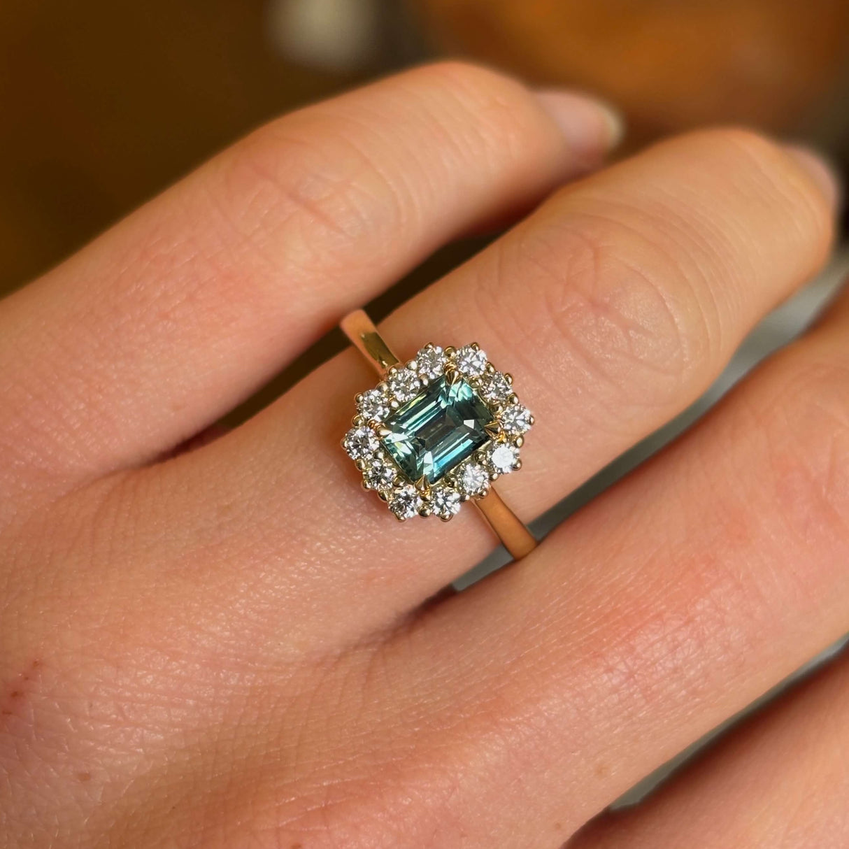 A yellow gold green sapphire and diamond cluster engagement ring worn on hand, close up to show the colour of the gemstone.