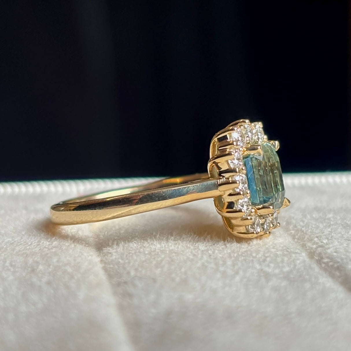 A yellow gold green sapphire and diamond cluster engagement ring worn on hand, close up to show the colour of the gemstone.