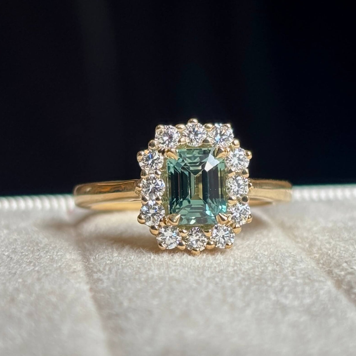A yellow gold green sapphire and diamond cluster engagement ring worn on hand, close up to show the colour of the gemstone.