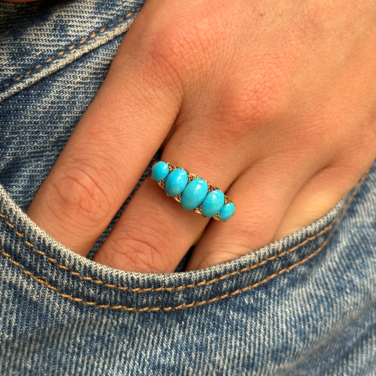 turquoise five stone half hoop ring, worn on hand and placed in pocket of jeans, front view.