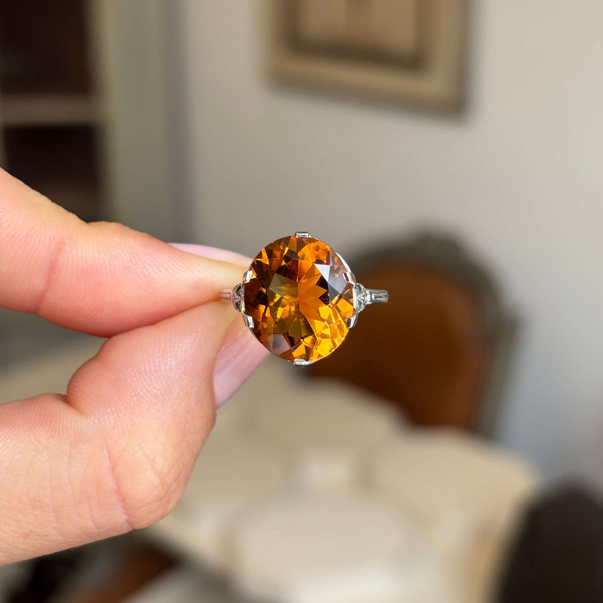Hand holding a platinum Antique, Art Deco citrine cocktail ring against a blurred indoor background