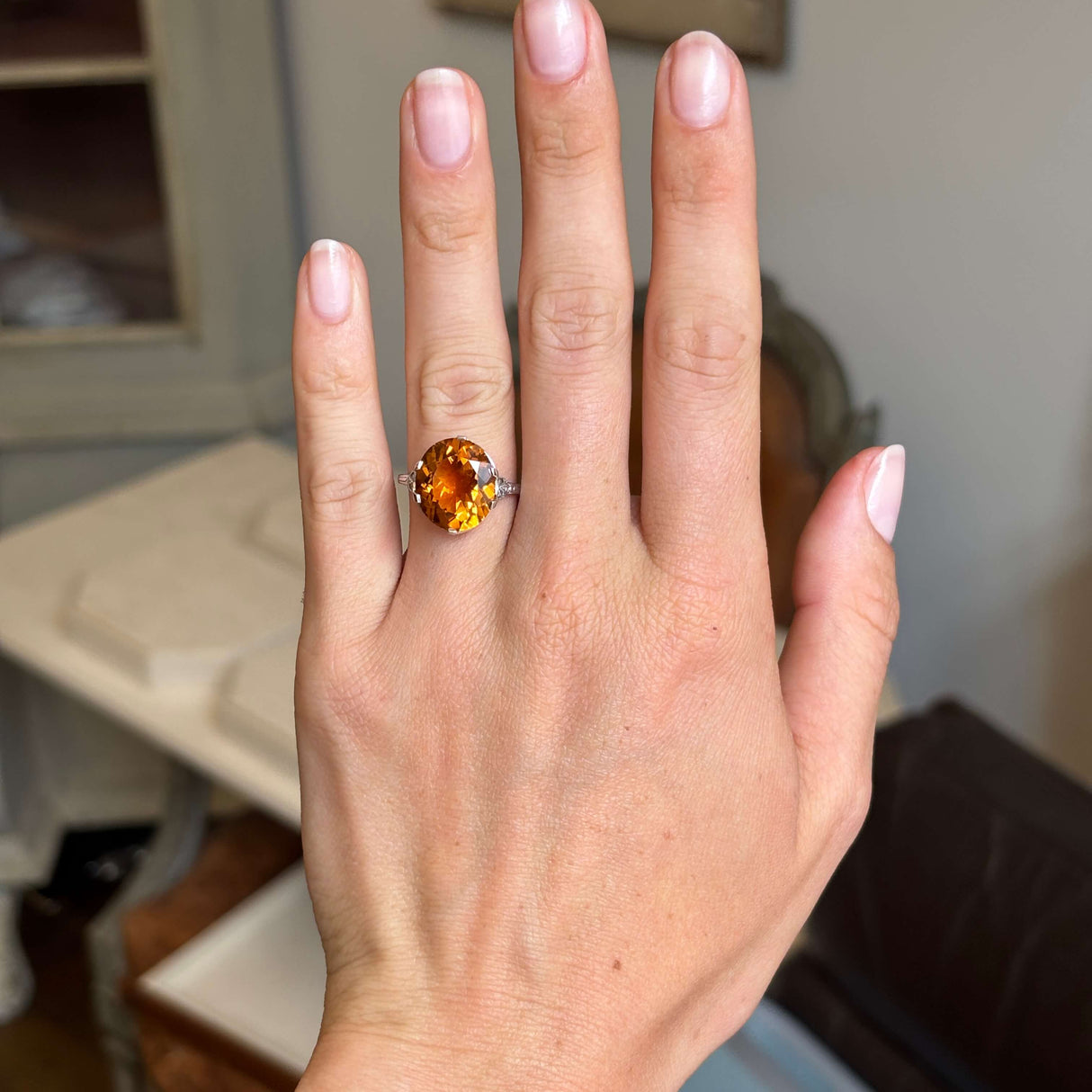 Hand wearing an Antique, Art Deco citrine cocktail ring in platinum against a blurred indoor background
