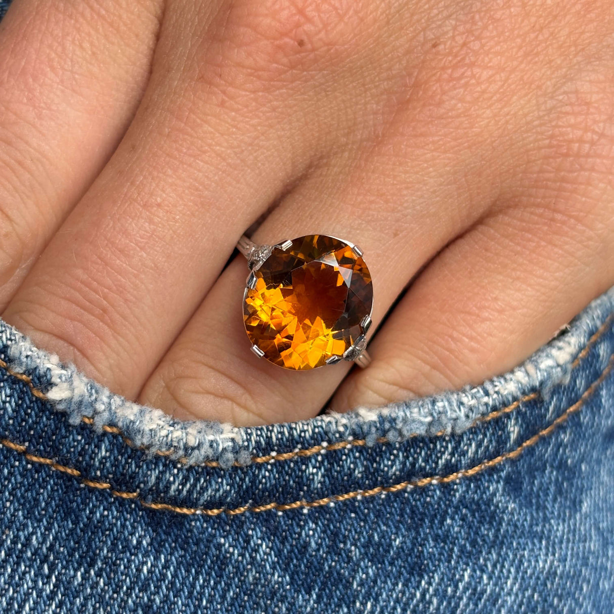 Close-up of a hand wearing an Antique, Art Deco citrine cocktail ring in platinum on denim fabric.