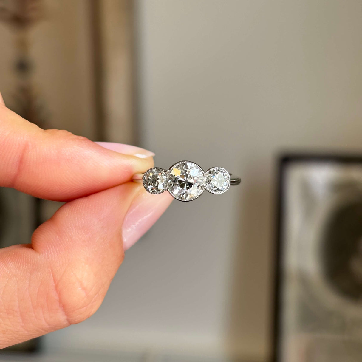 Hand holding an Antique, Art Deco old-cut diamond three-stone platinum ring against a blurred background