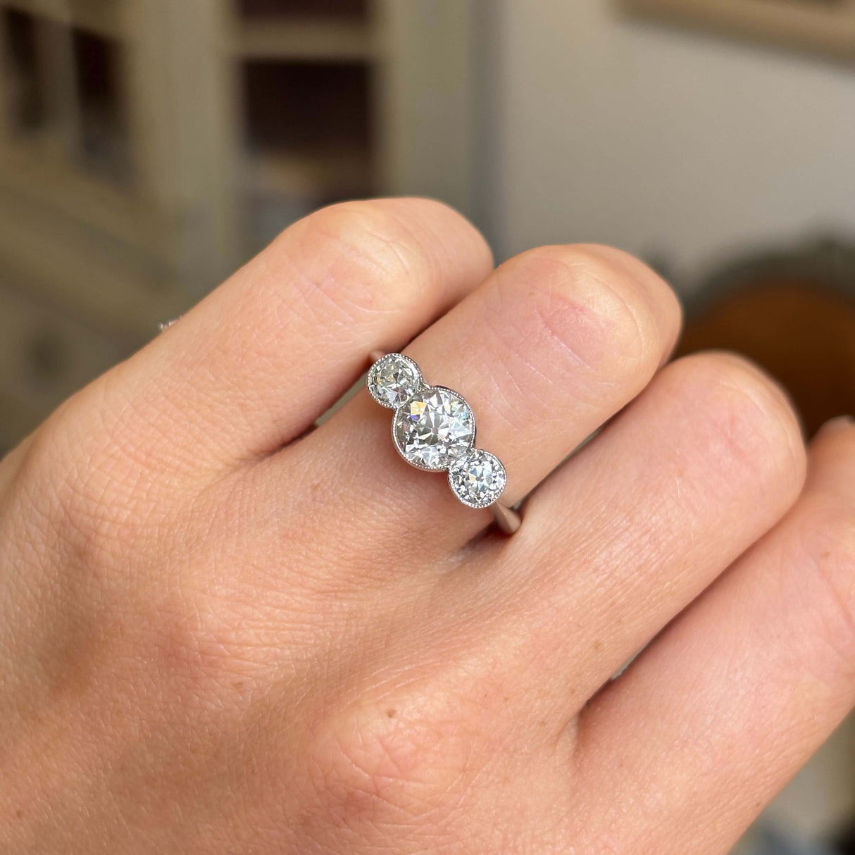 Platinum Antique Art Deco diamond engagement ring with three old-cut diamonds worn on a hand against a blurred background