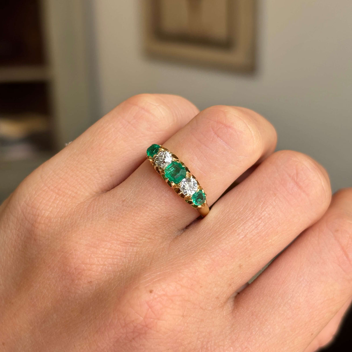 Gold Antique, Victorian emerald & old-mine diamond five-stone engagement ring on a hand against a neutral background