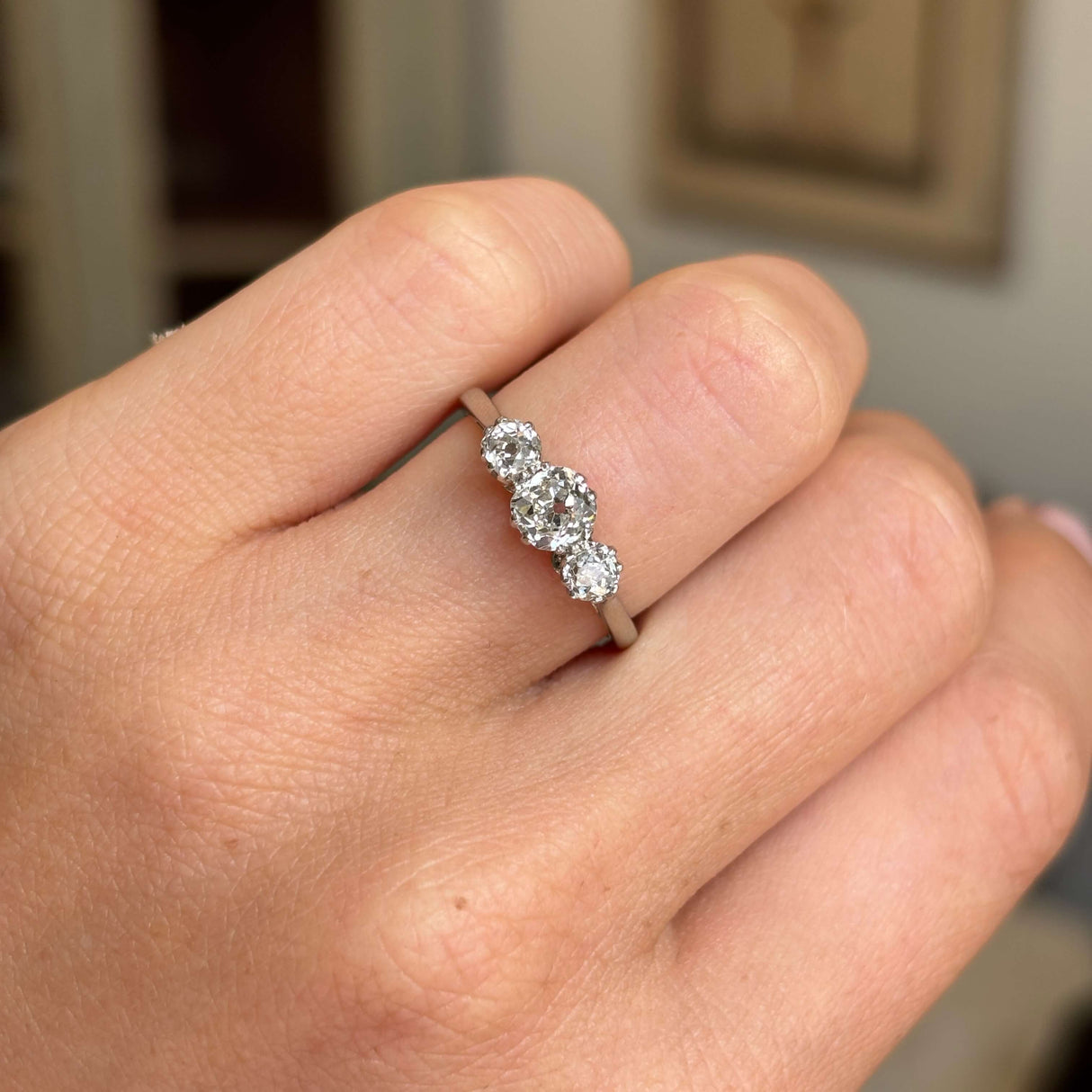 Vintage, 1940s old-mine cut diamond three-stone engagement ring in white gold worn on a hand against a blurred background