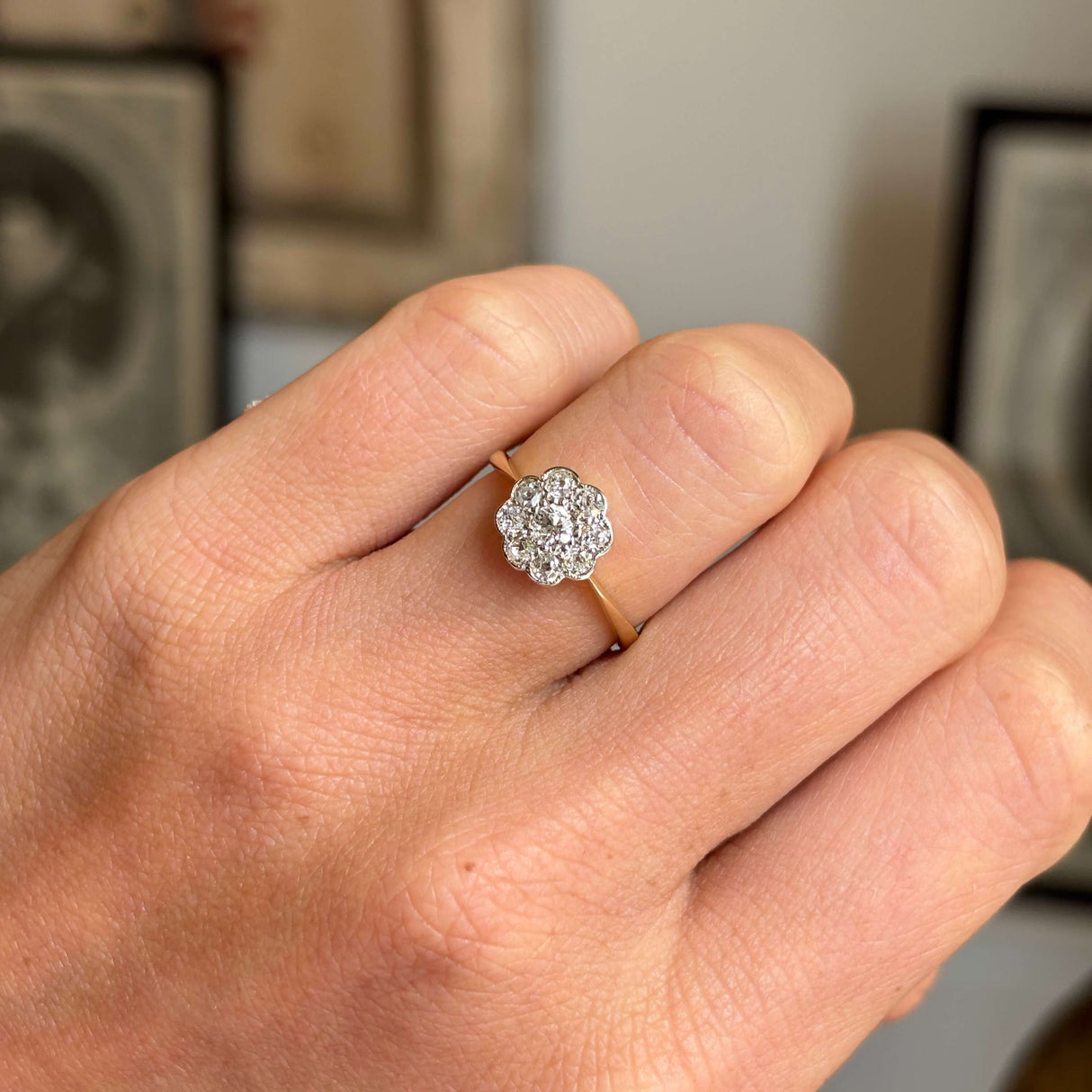 Hand wearing an Antique, Edwardian old-cut diamond cluster ring in yellow gold with a blurred background